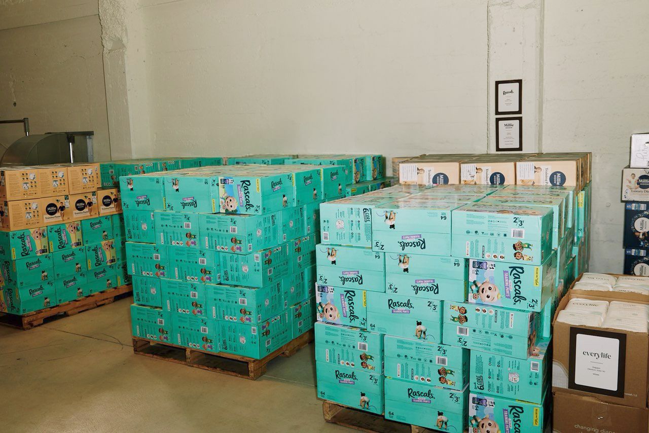 Woman holding donation box container numerous products, including Rascals nappies, a unicorn and various toys.