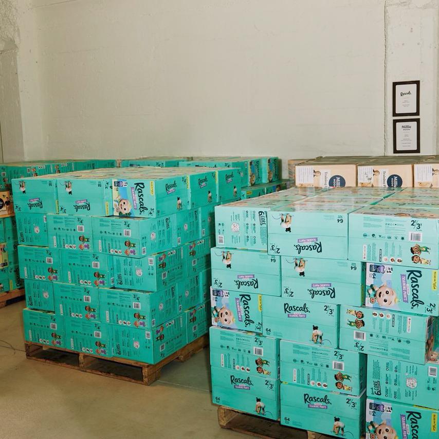 Woman holding donation box container numerous products, including Rascals nappies, a unicorn and various toys.