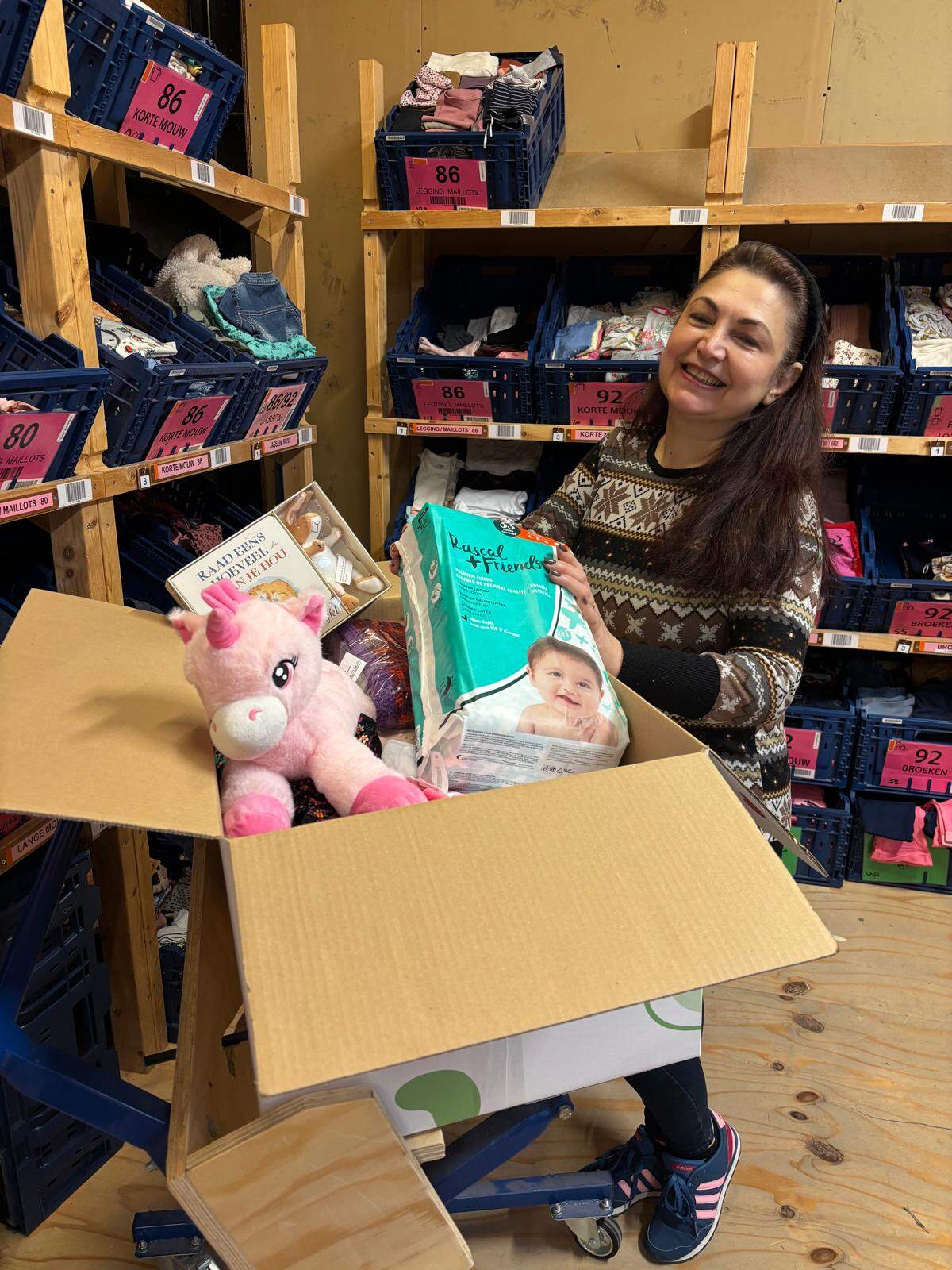 Woman holding donation box container numerous products, including Rascals nappies, a unicorn and various toys.