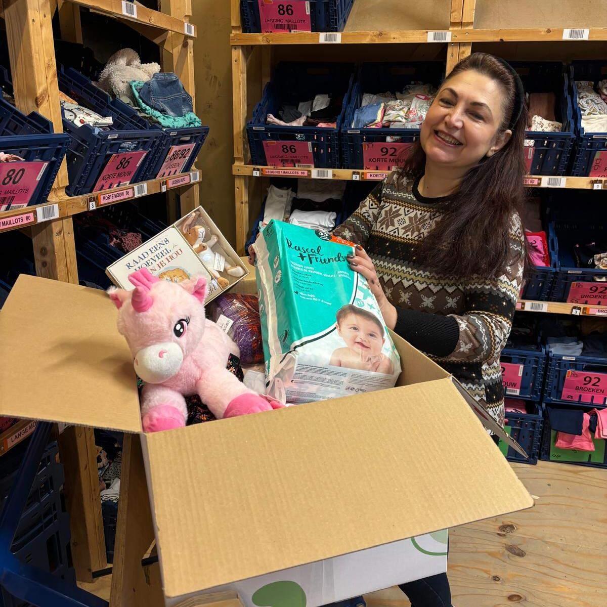 Woman holding donation box container numerous products, including Rascals nappies, a unicorn and various toys.