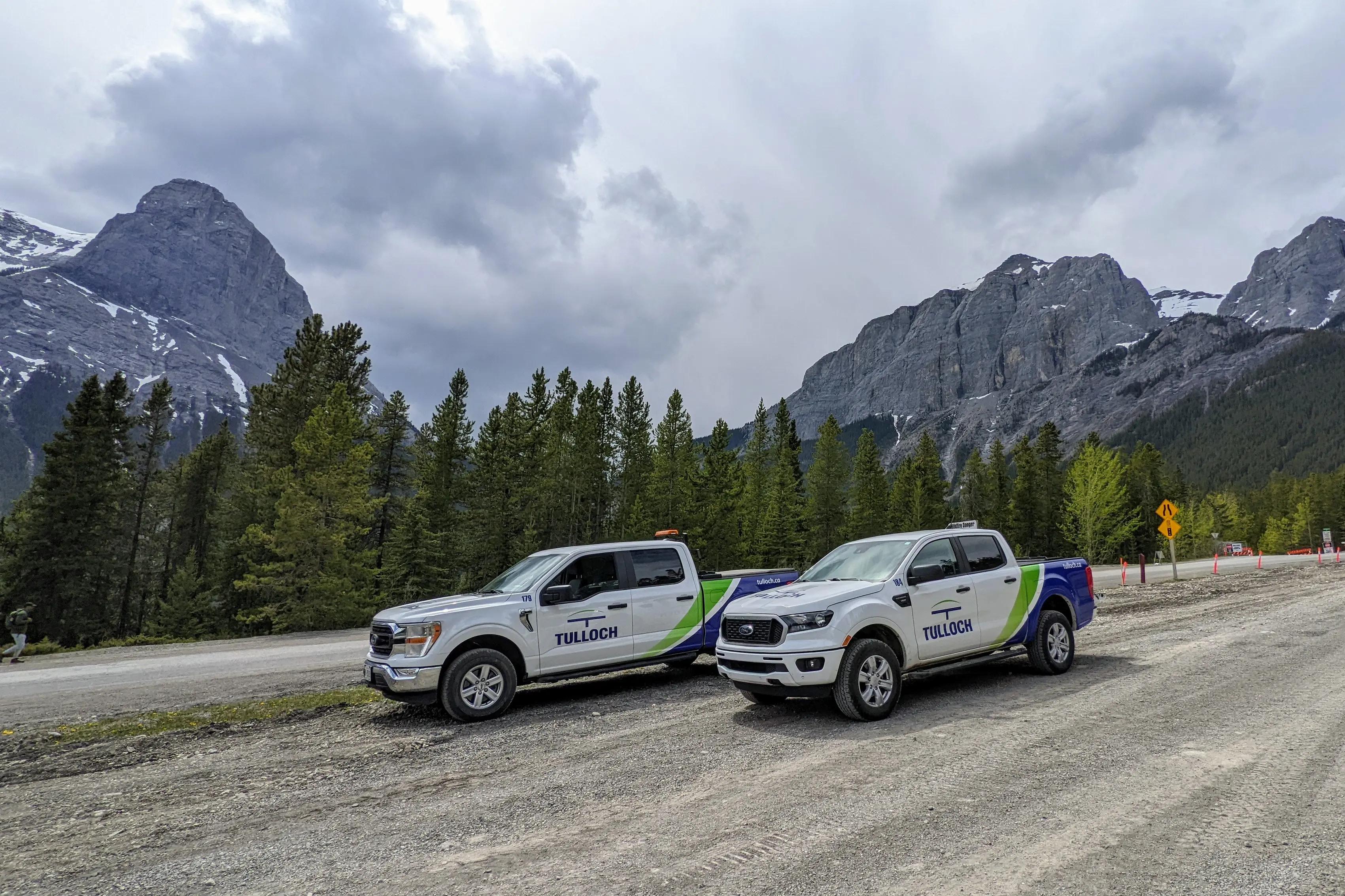 Two TULLOCH company trucks parked along a mountain roadway in Alberta.