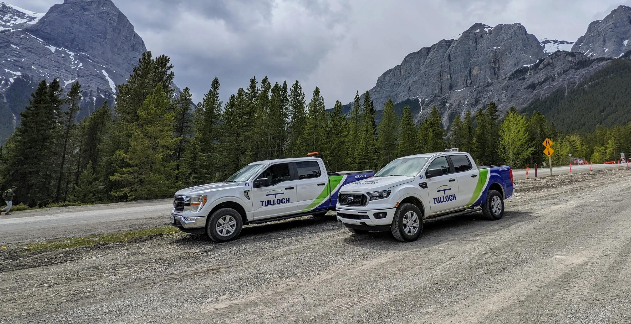 Two TULLOCH company trucks parked along a mountain roadway in Alberta.