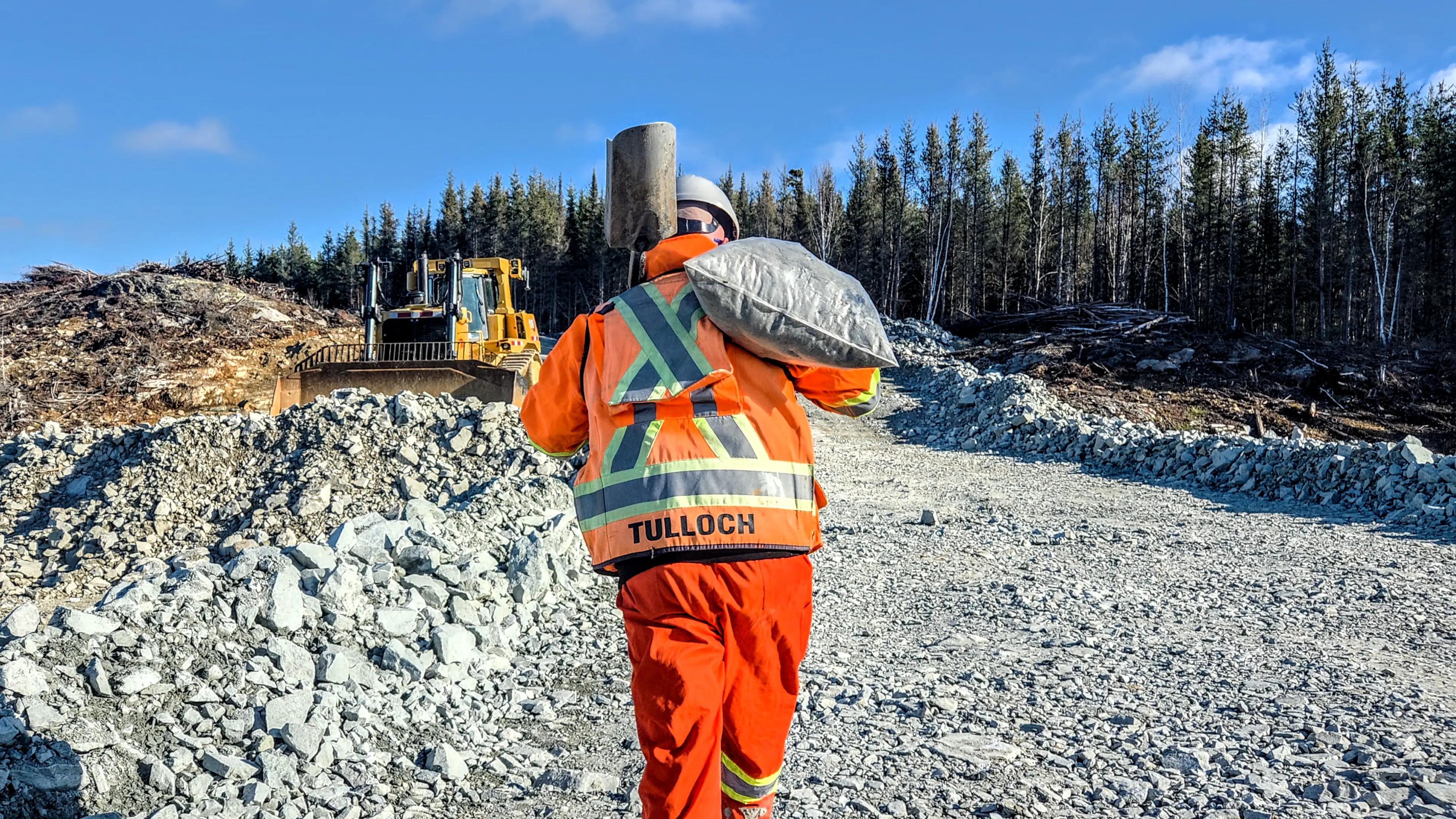TULLOCH surveyor walking across a rocky mine site with survey equipment.