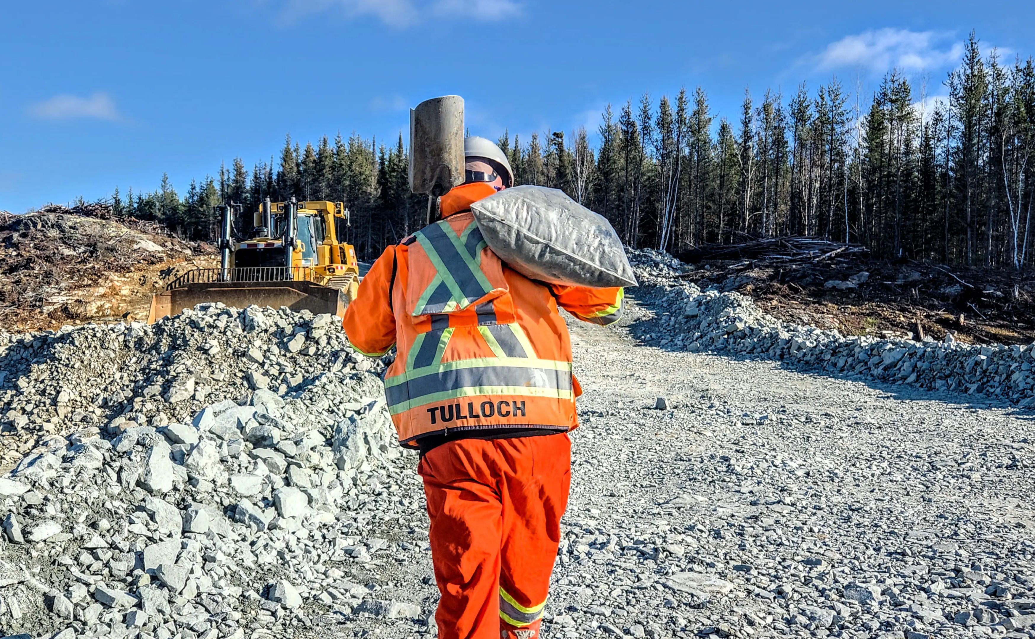 TULLOCH surveyor walking across a rocky mine site with survey equipment.