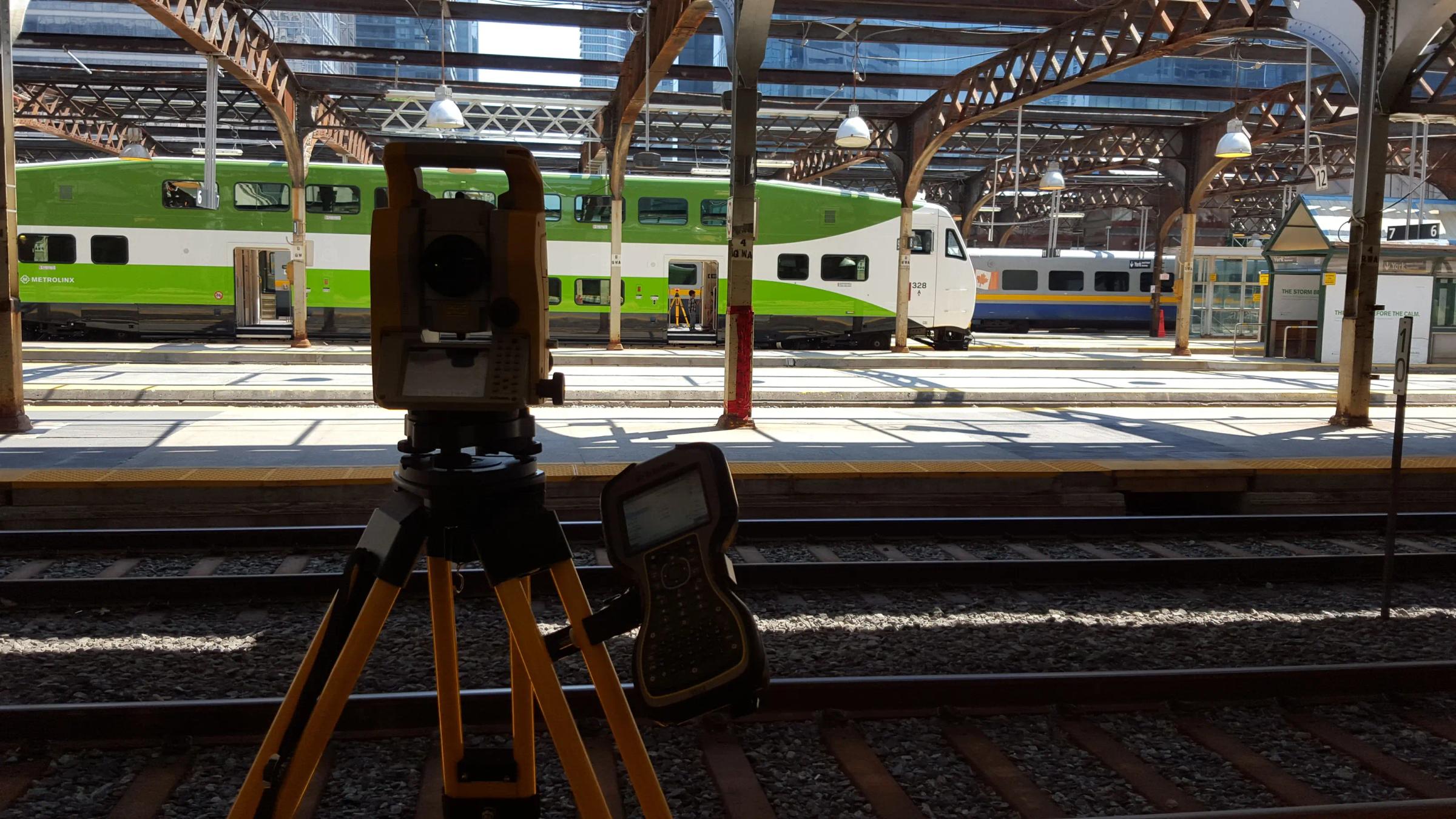 Survey equipment set up beside GO Transit rail infrastructure at a station.