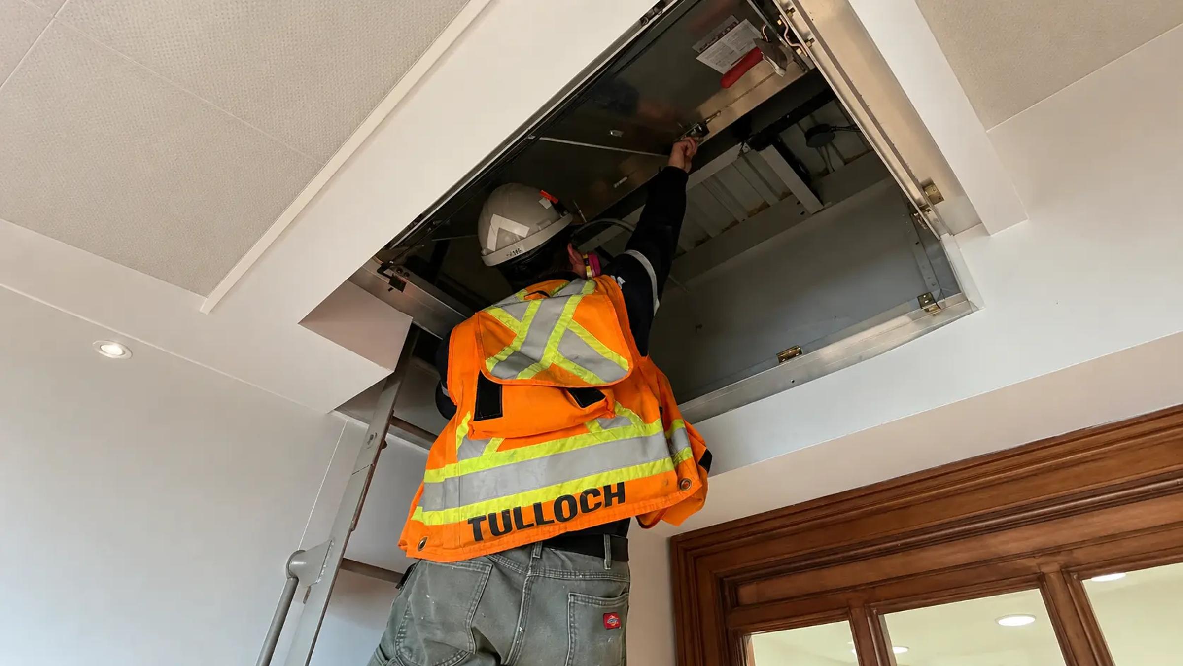 TULLOCH building inspection technician reviewing an overhead building component.