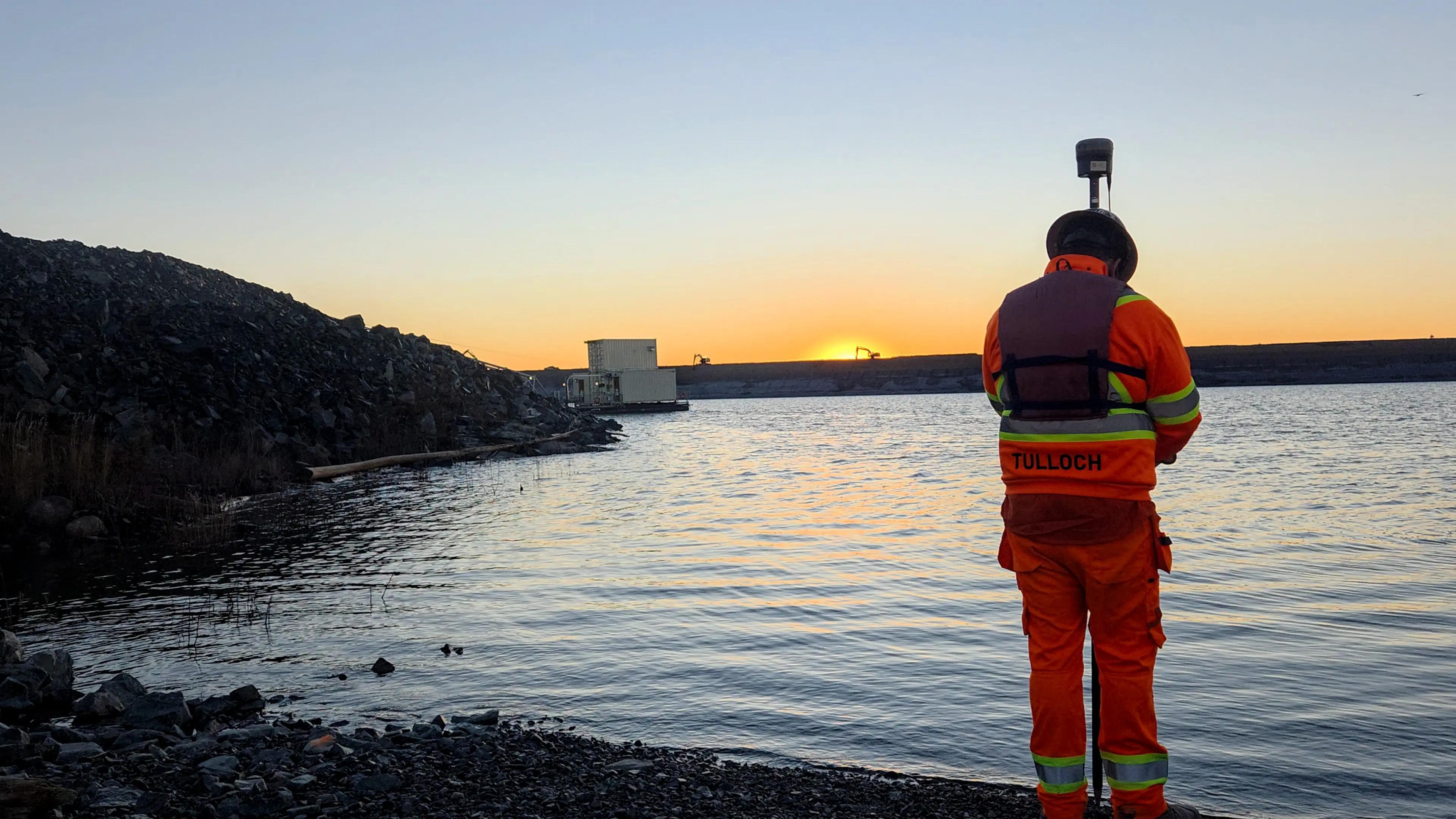TULLOCH surveyor collecting field data beside a waterbody at sunset.