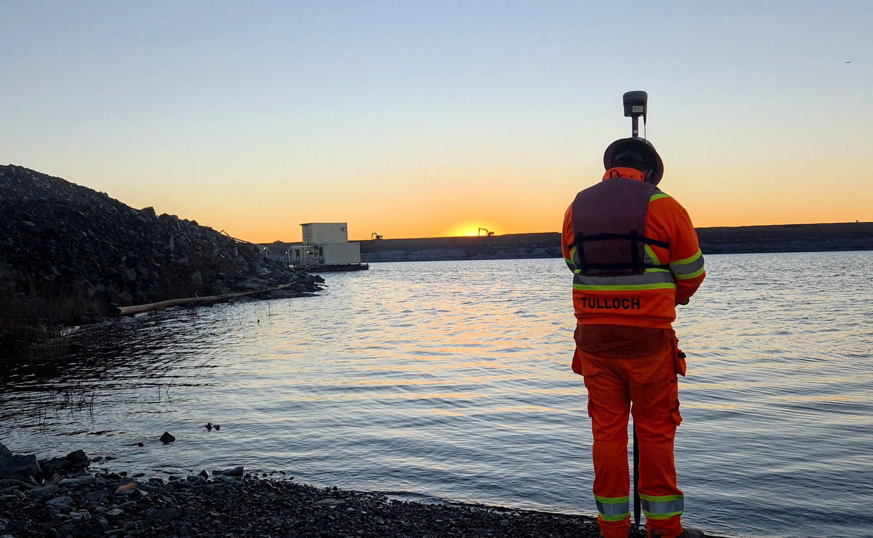 TULLOCH surveyor collecting field data beside a waterbody at sunset.