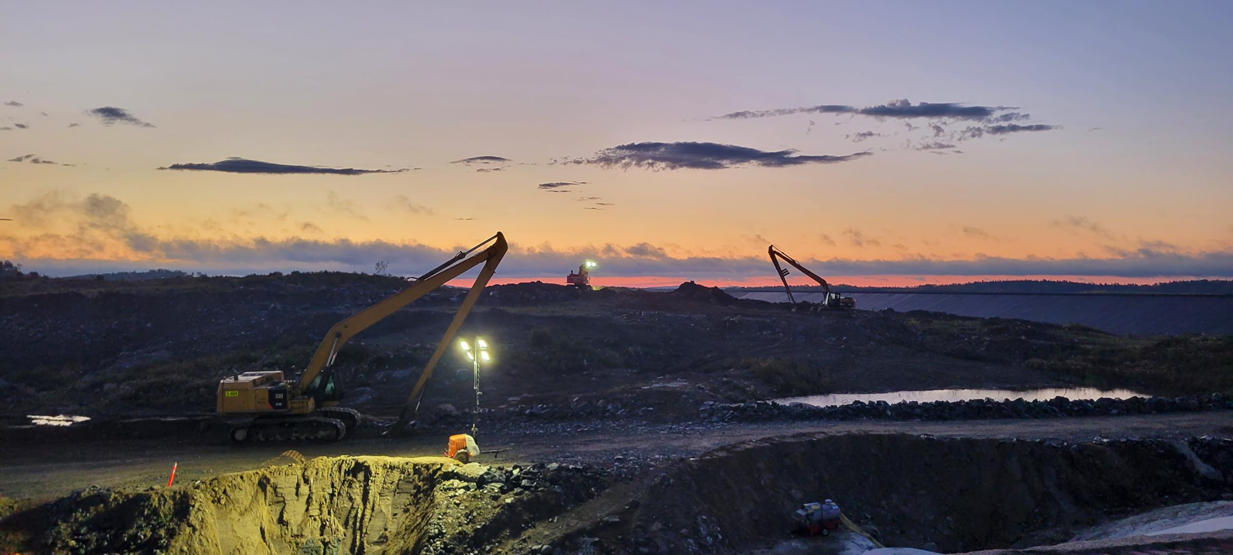 Mining site viewed at sunset with illuminated processing areas.
