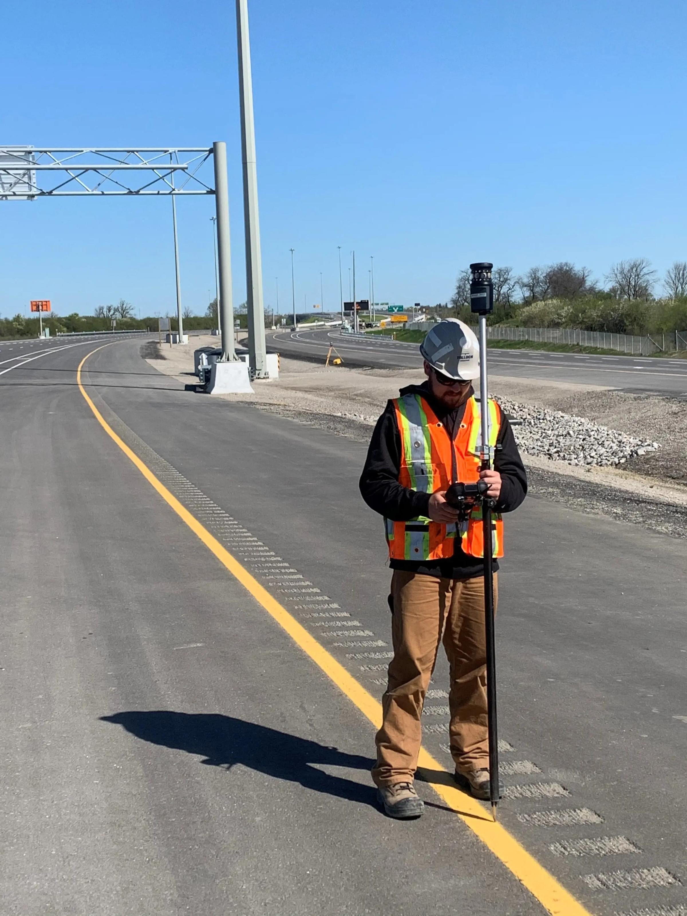 Survey technician collecting roadway data along Highway 401 in Ontario.