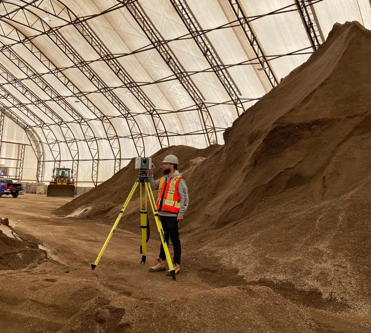 TULLOCH survey technician measuring a large indoor material stockpile.