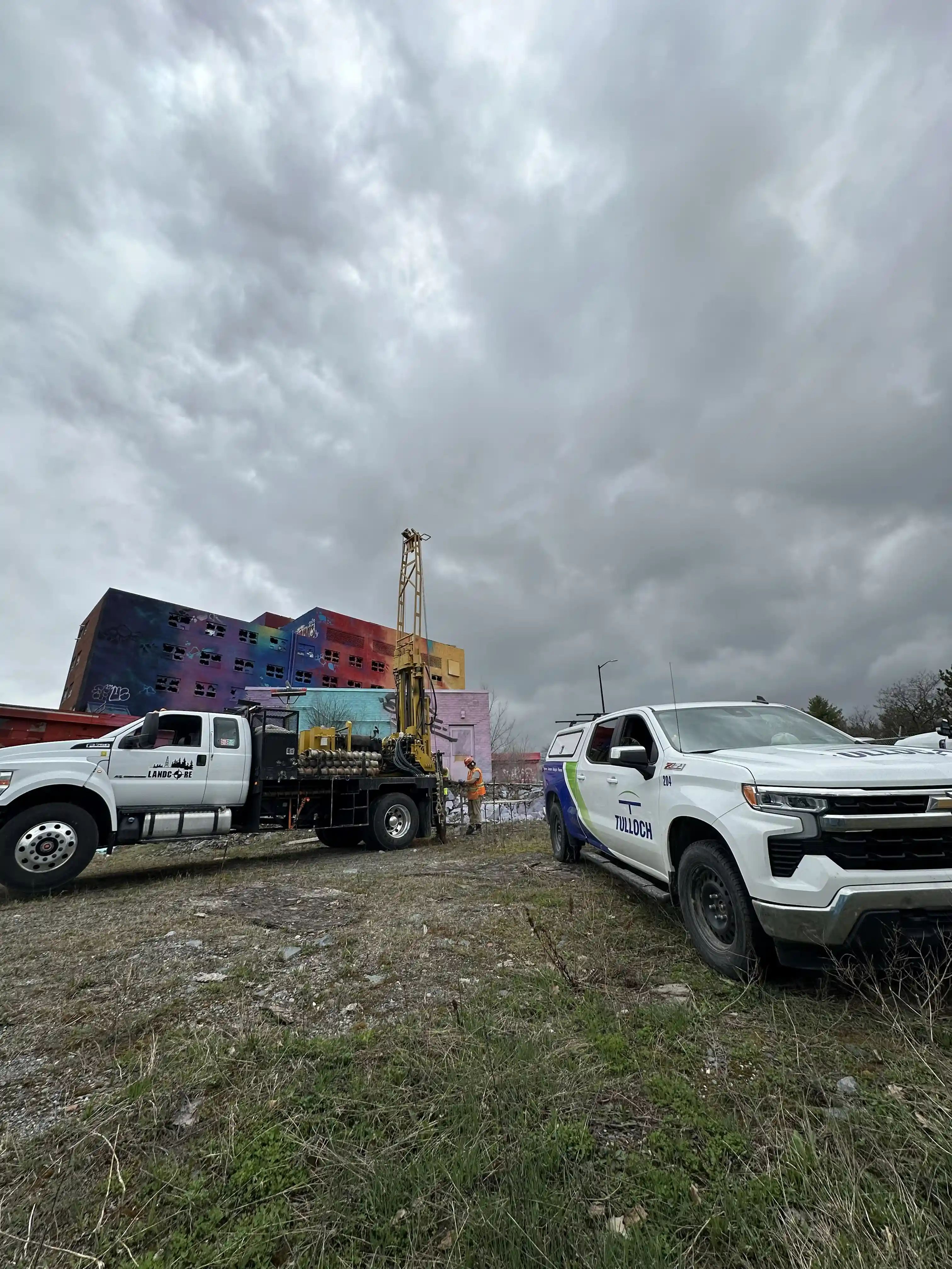 Geotechnical drilling rig and field vehicles at a General Hospital project site.