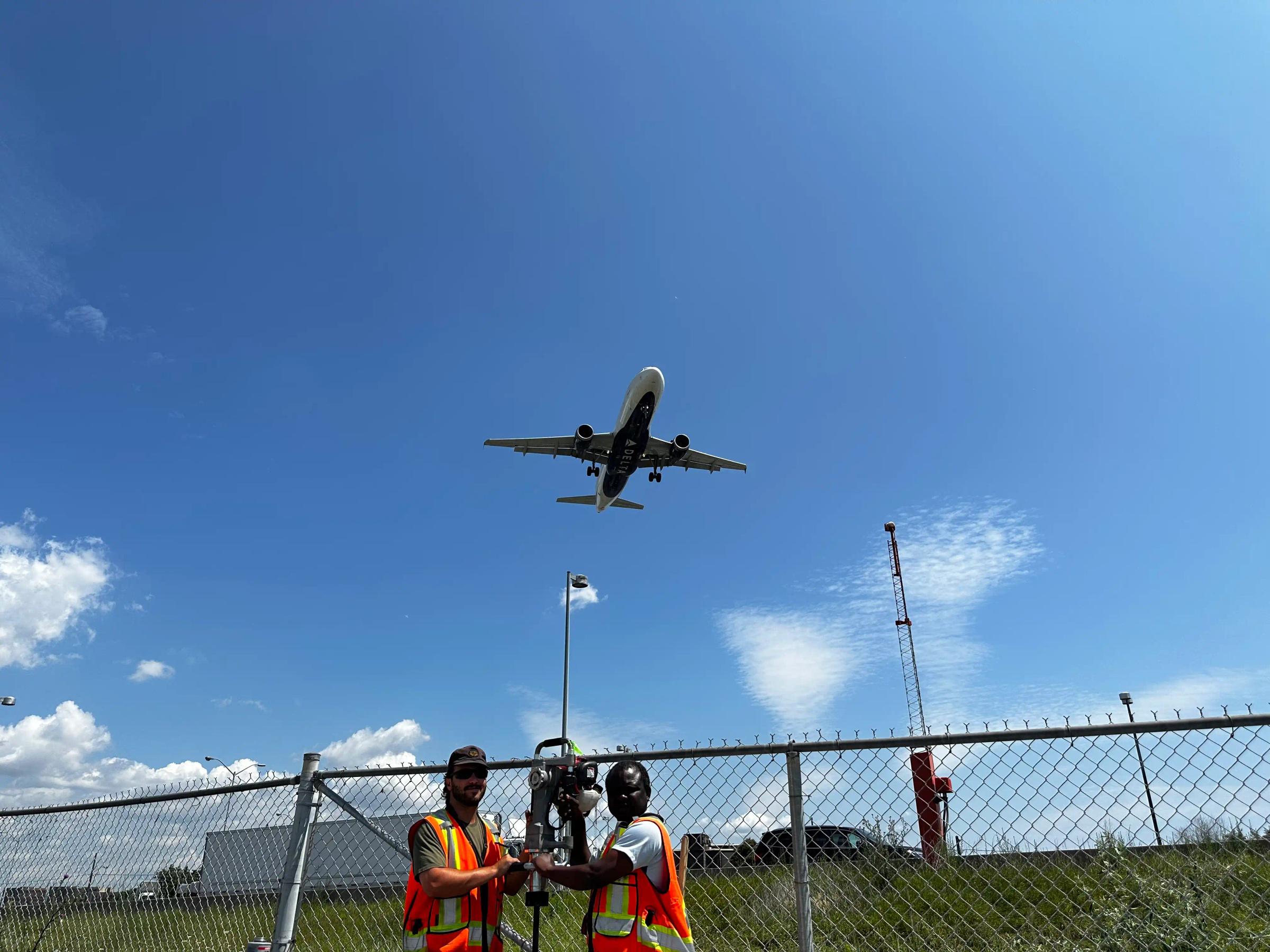 Survey crew working near an aircraft hangar and active airfield.