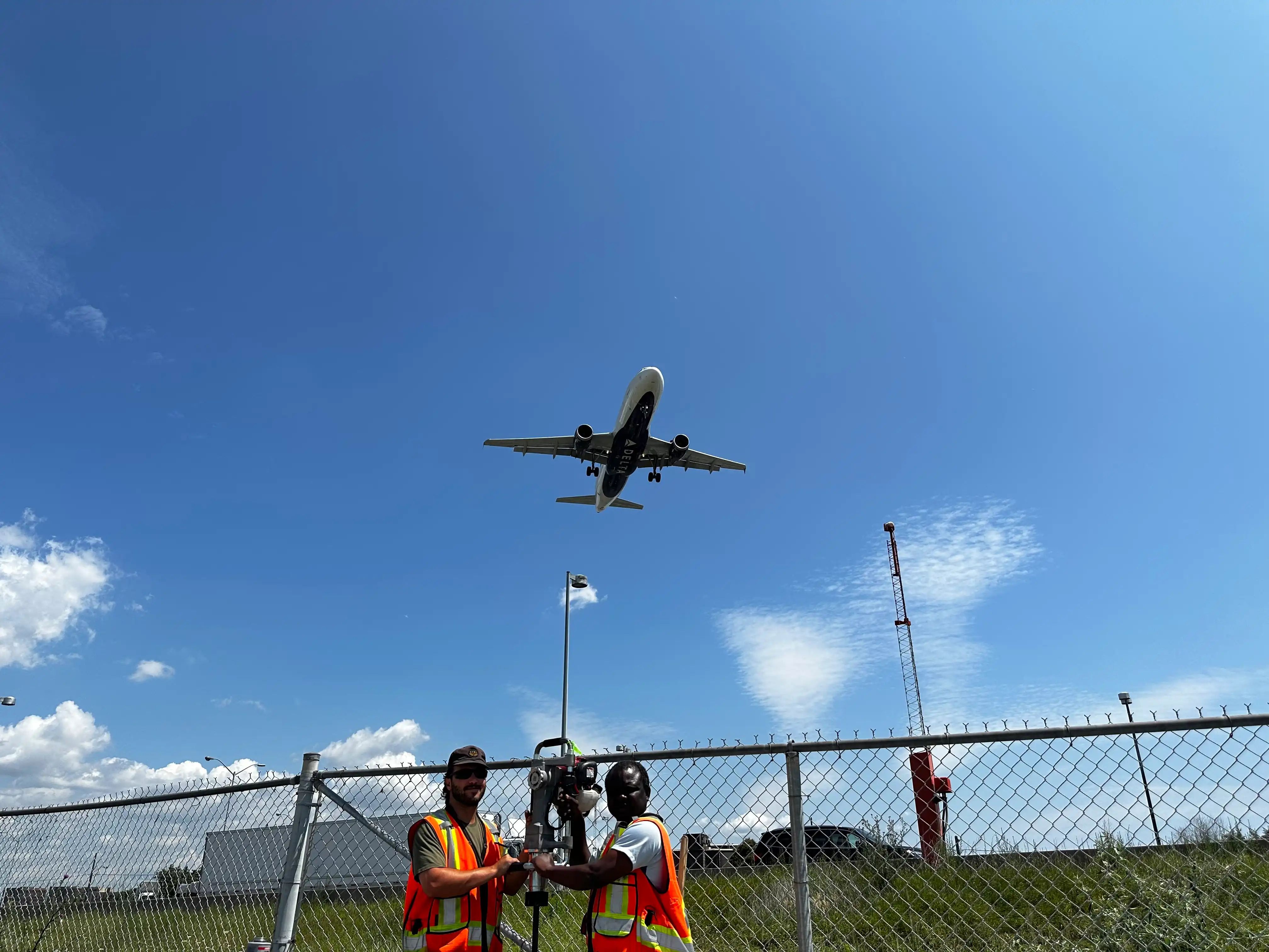 Survey crew working near an aircraft hangar and active airfield.