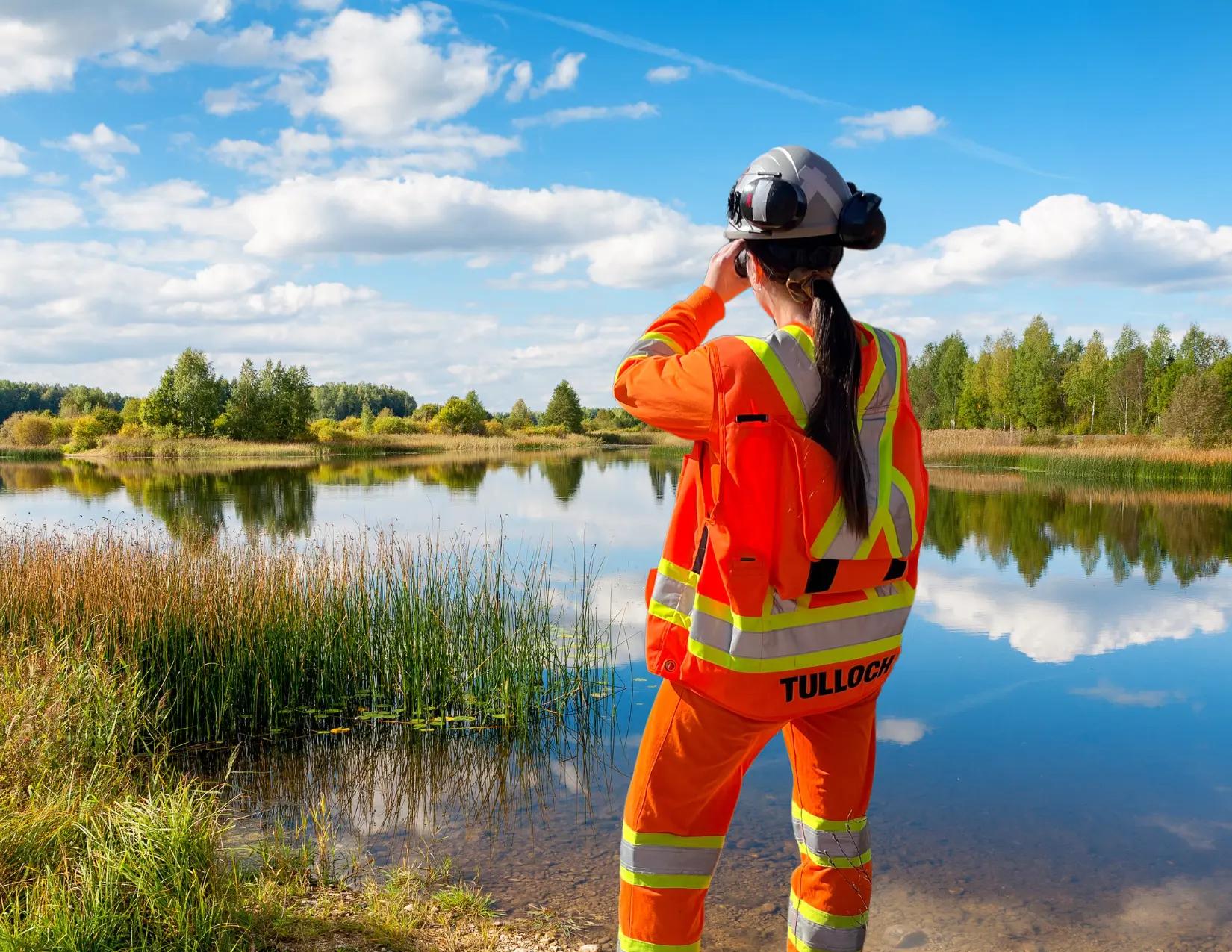 TULLOCH environmental field technician using binoculars beside a wetland or waterbody.