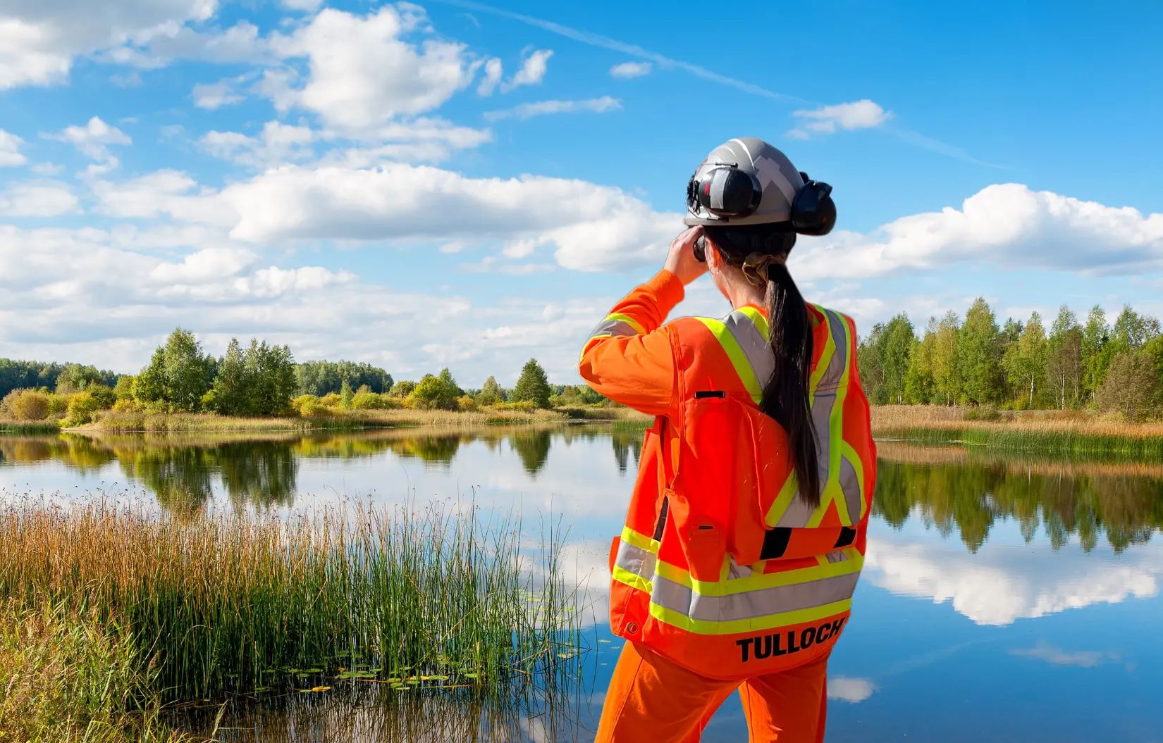 TULLOCH environmental field technician using binoculars beside a wetland or waterbody.