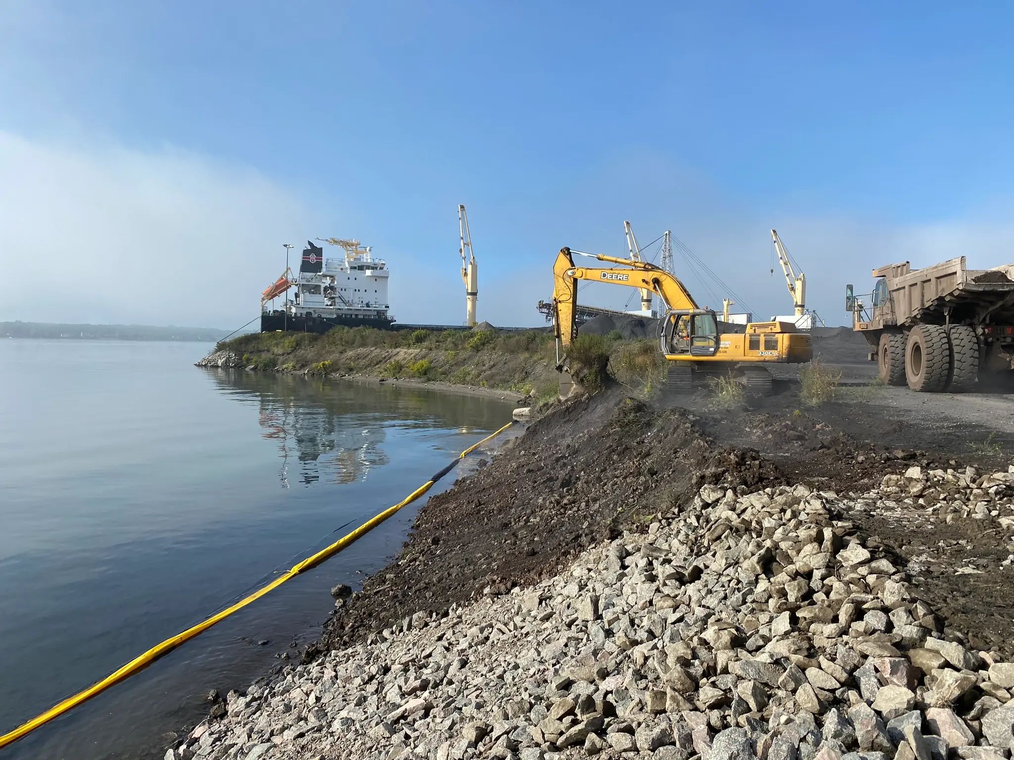Excavator completing shoreline grading beside the water.