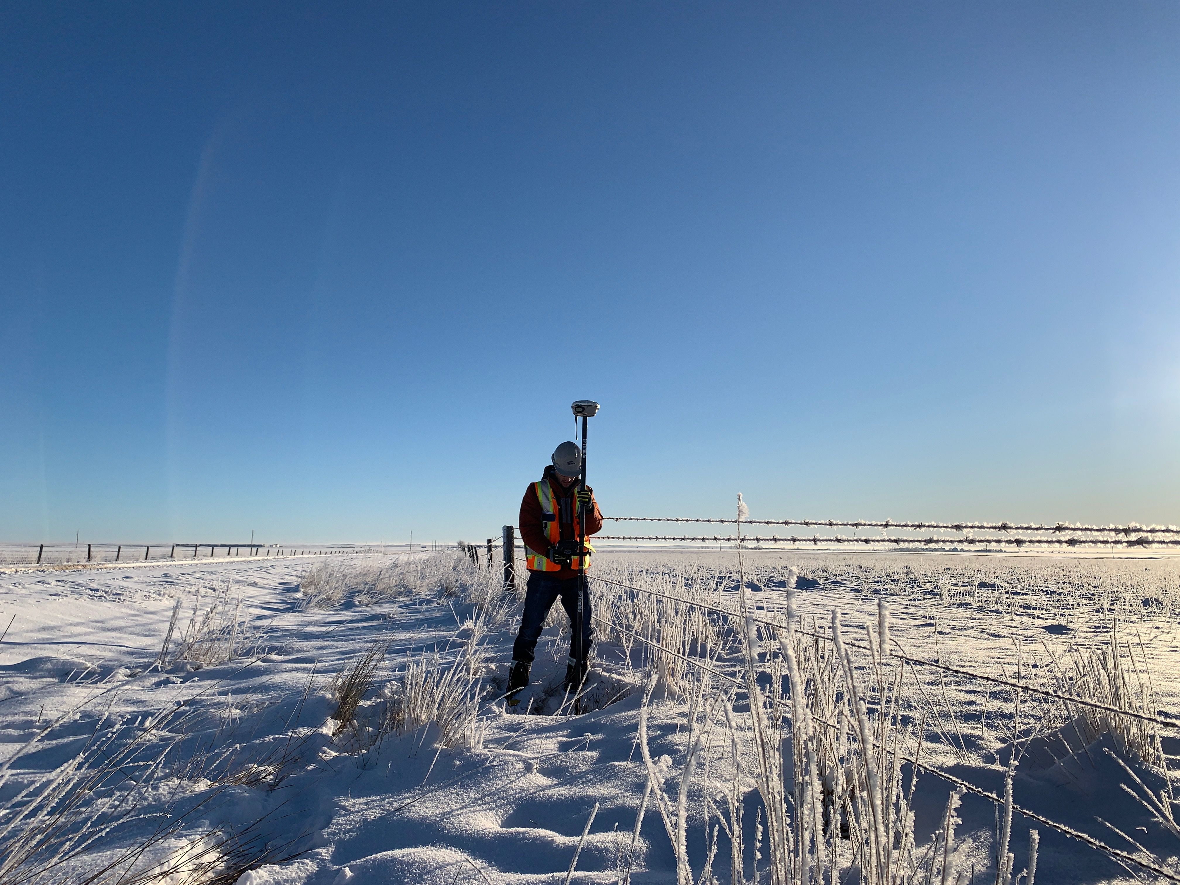 TULLOCH field surveyor working with survey equipment across snow-covered open terrain.