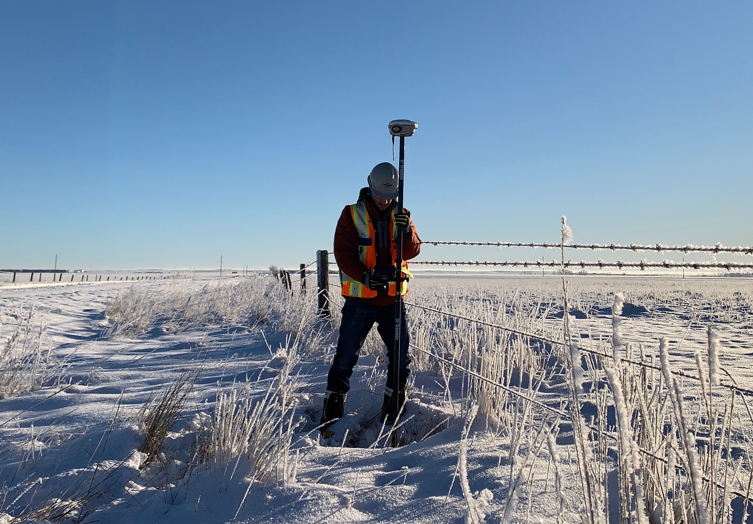 TULLOCH field surveyor working with survey equipment across snow-covered open terrain.