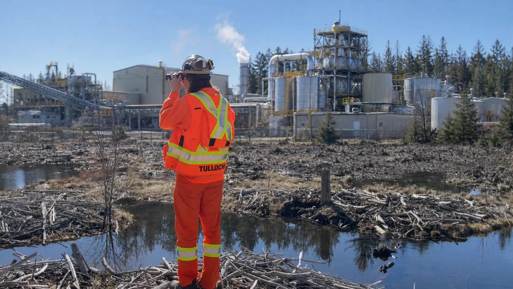 Field specialist in high-visibility PPE reviewing conditions at an industrial site.