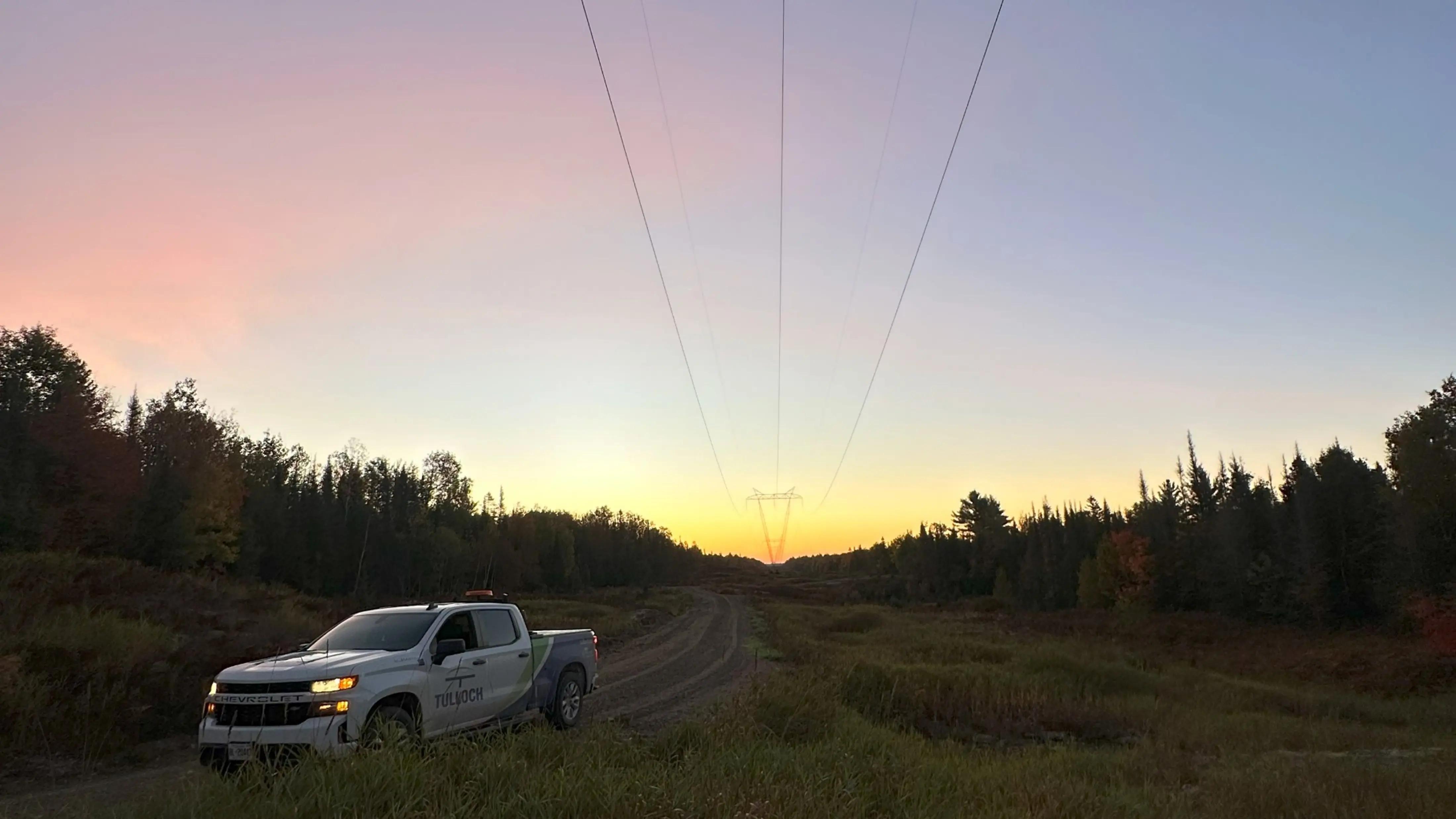 TULLOCH company truck beneath transmission lines at sunset.