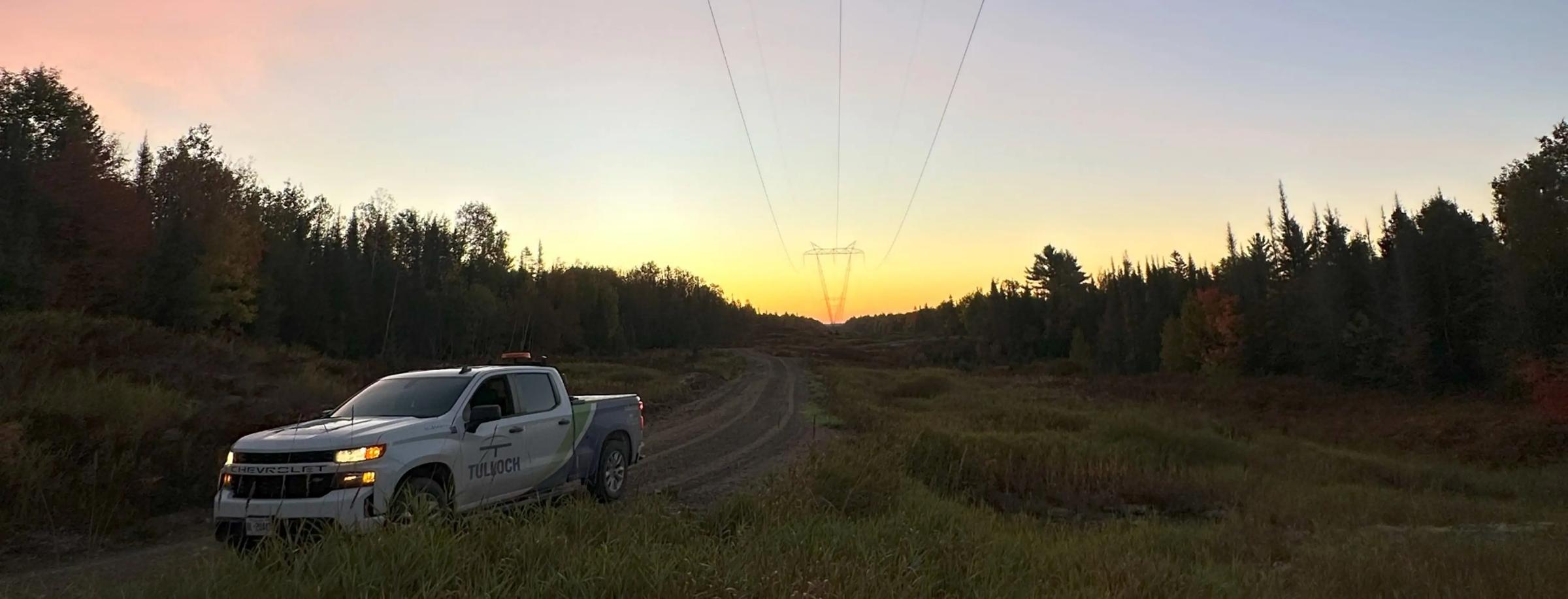 TULLOCH company truck beneath transmission lines at sunset.