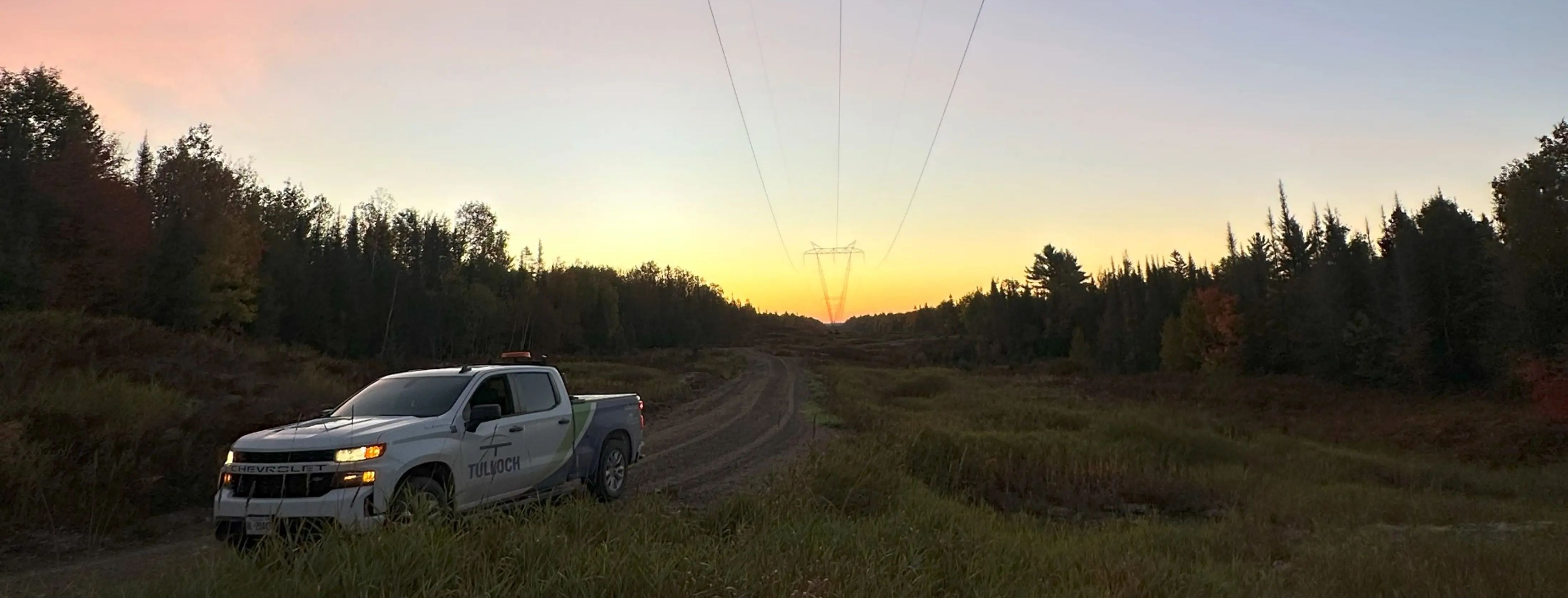 TULLOCH company truck beneath transmission lines at sunset.