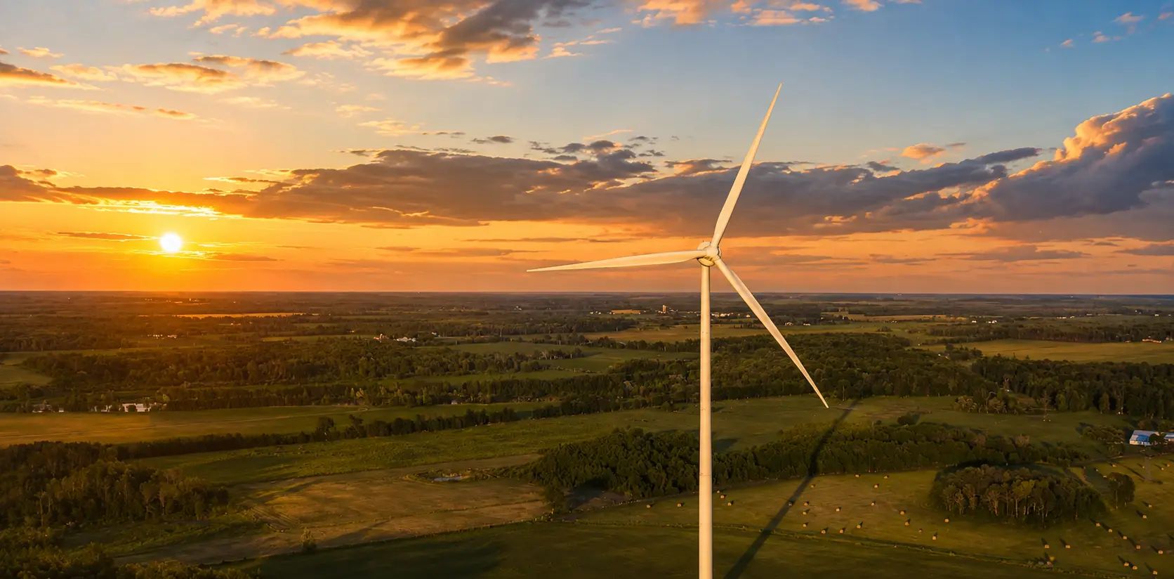 Aerial view of wind turbines across rural terrain at sunset.