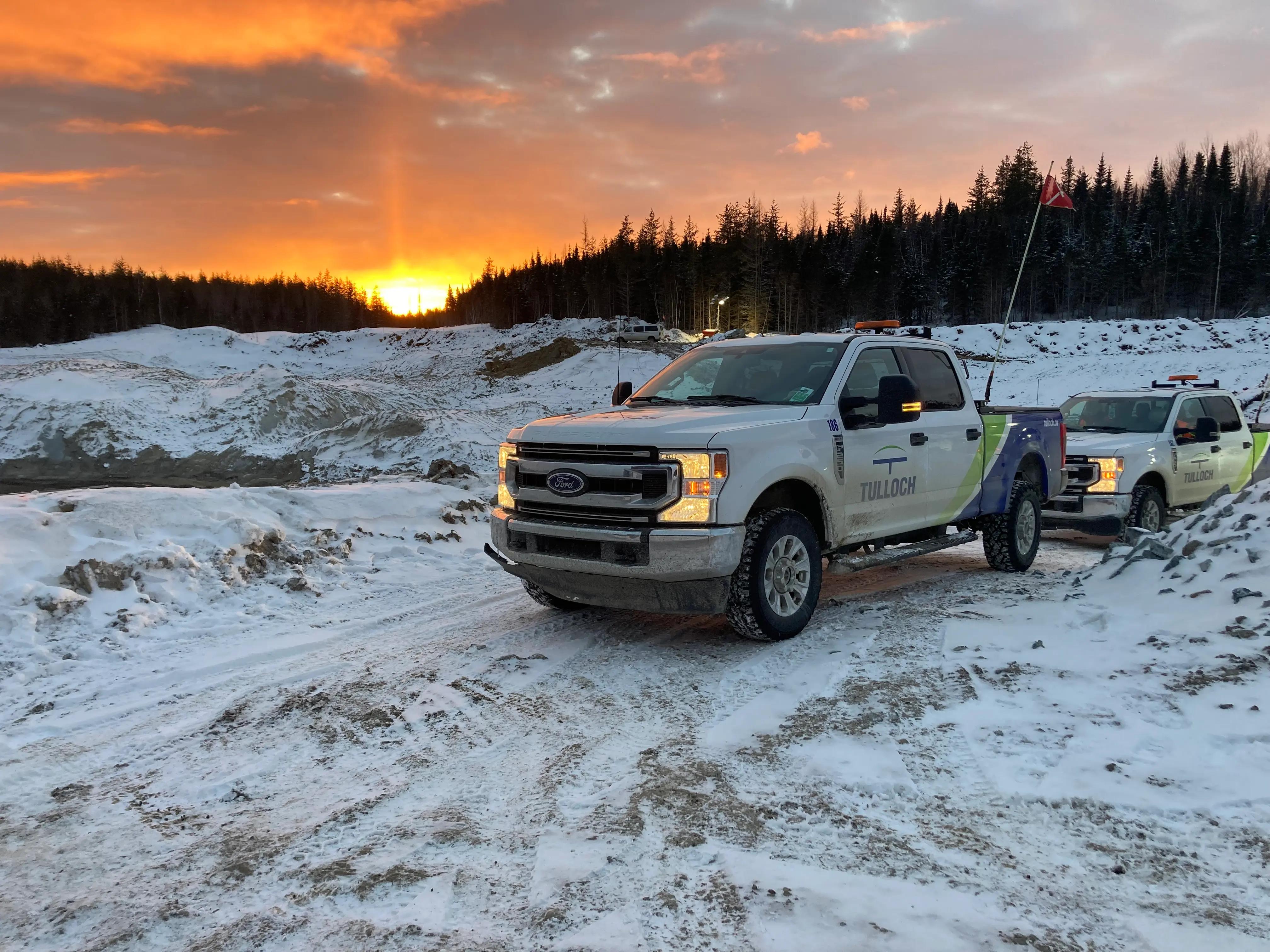 TULLOCH company trucks at a snowy project site during sunset.