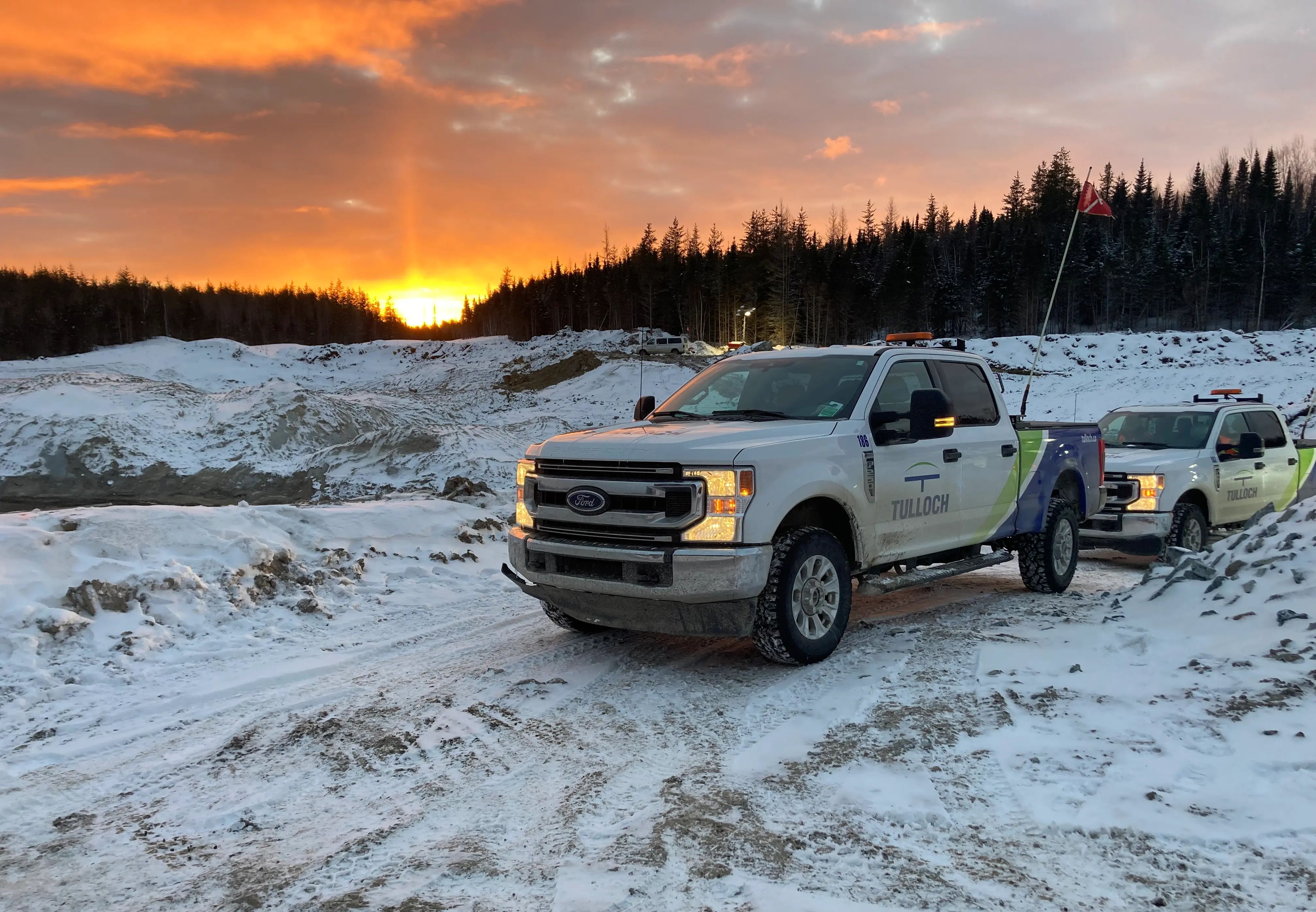 TULLOCH company trucks at a snowy project site during sunset.