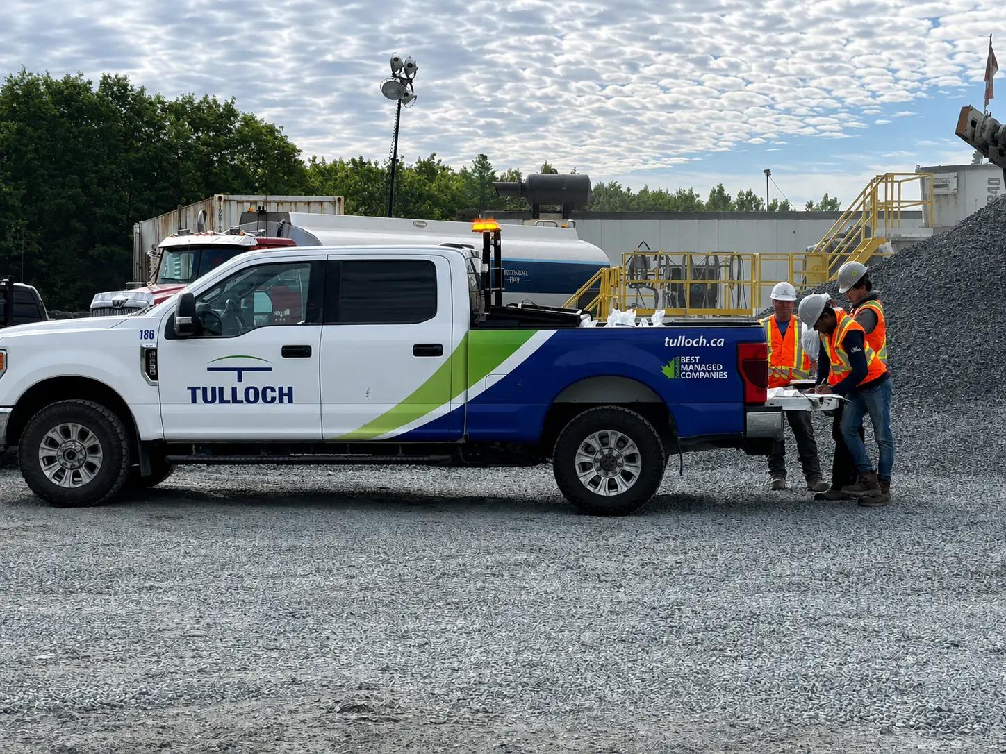 TULLOCH field crew reviewing project drawings beside a company truck.