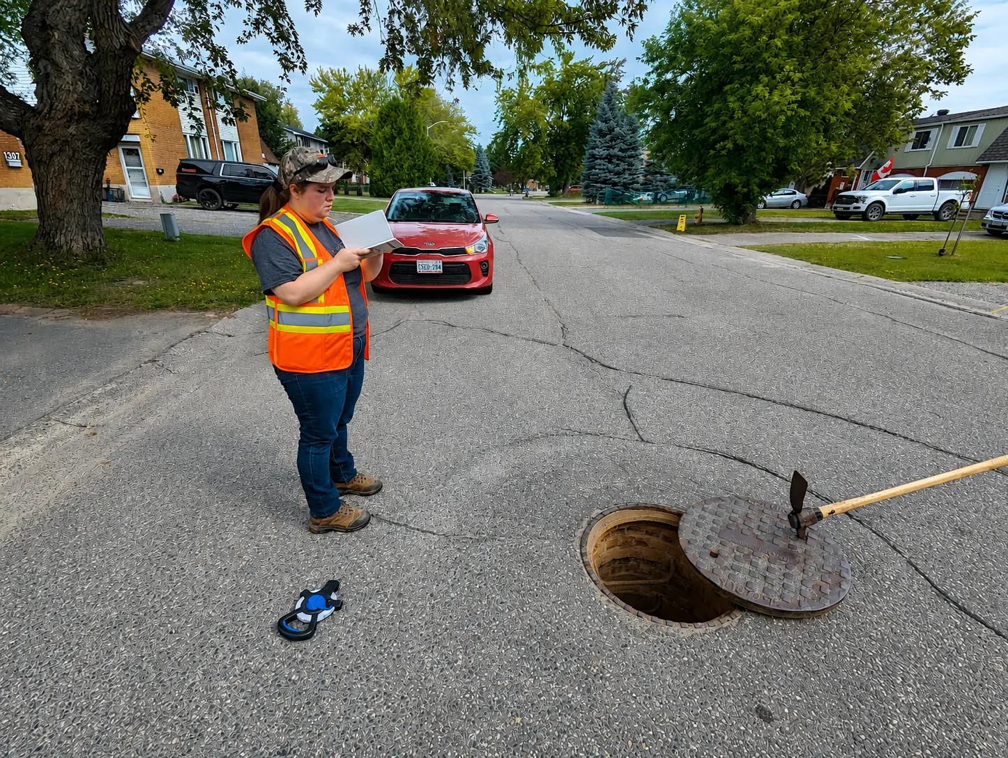 TULLOCH field technician completing roadway or sewer inspection work beside an access structure.