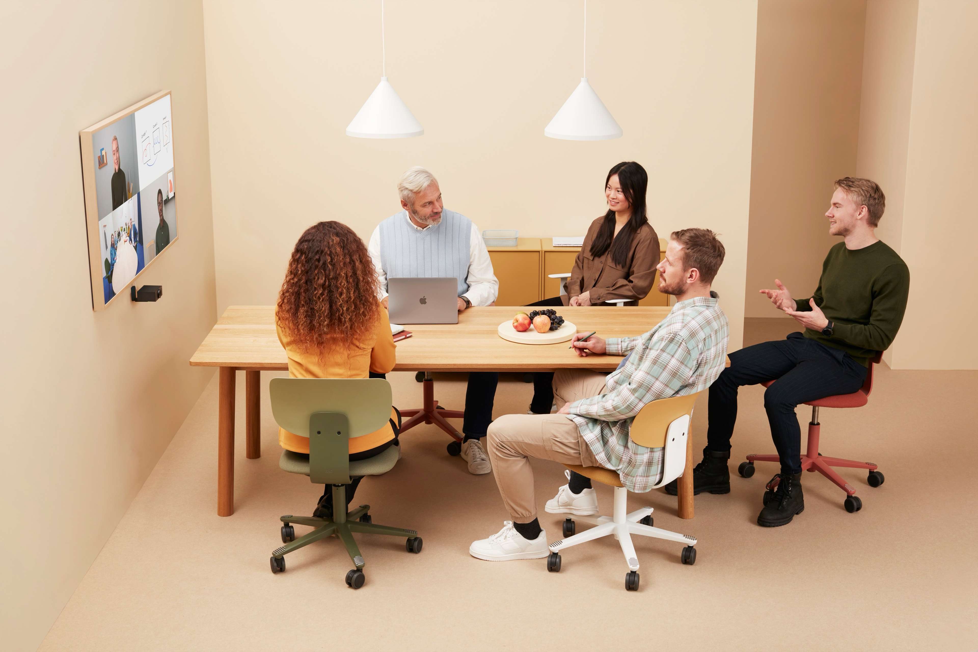 Five people in a meeting room, talking to online meeting participants