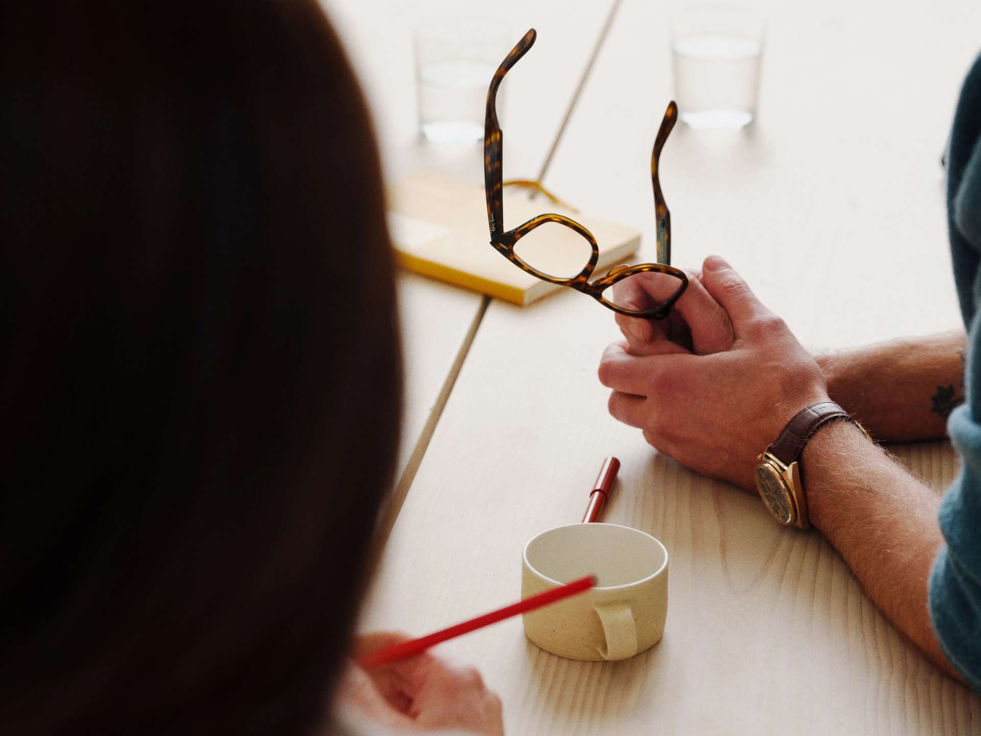 Man resting his arms on a desk, holding a pair of spectacles