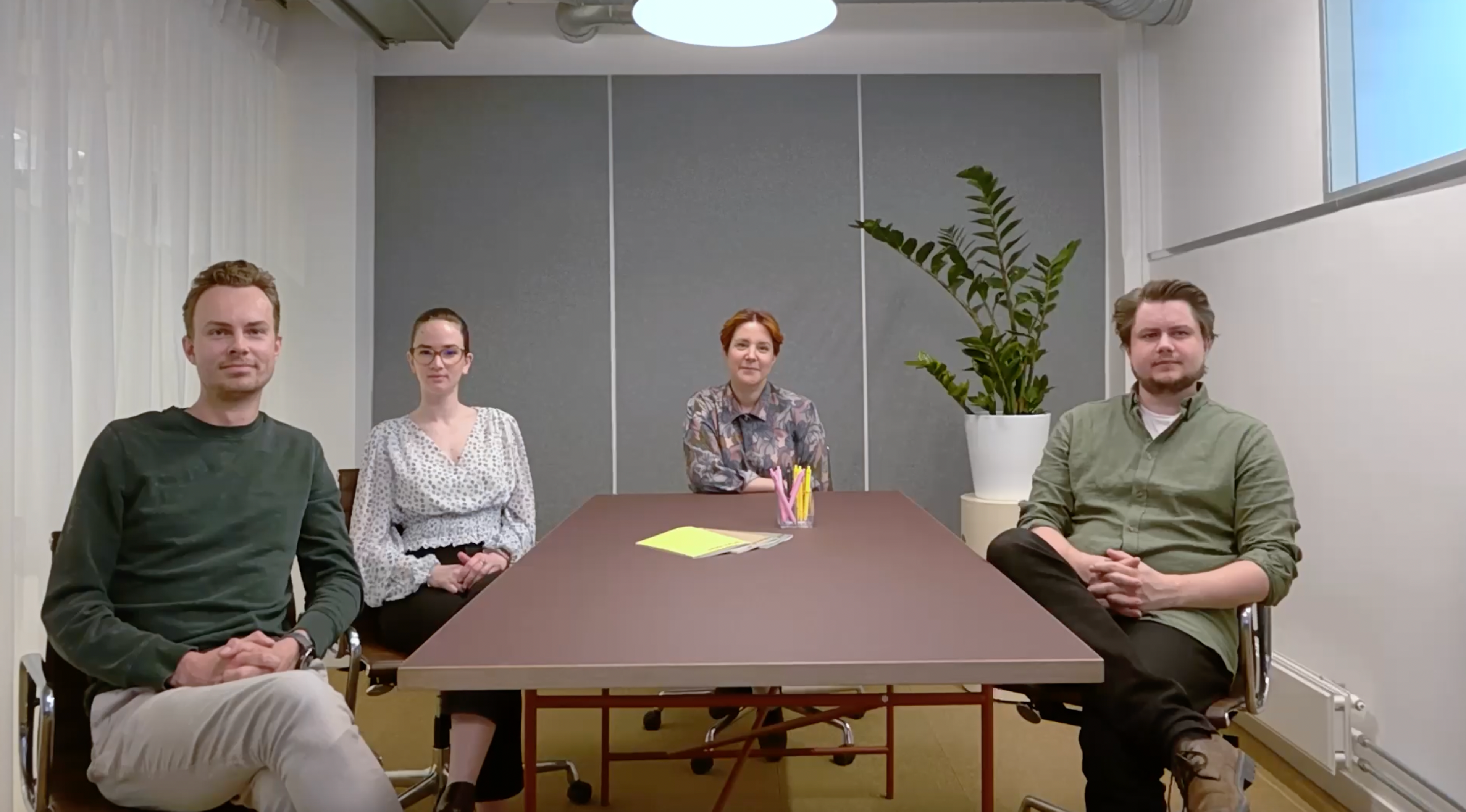 Four people in a meeting room, looking at the camera