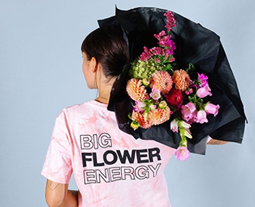 Woman facing backwards and holding a bouquet of flowers over her right shoulder. She is wearing a Floom t-shirt.