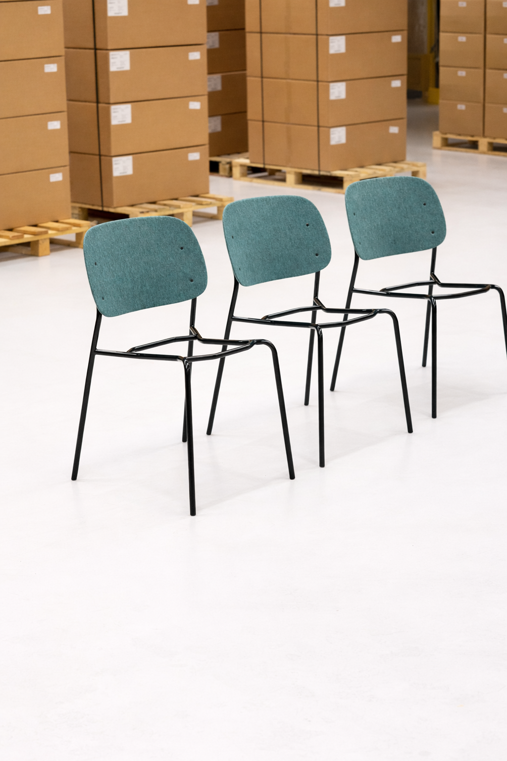 Three Hale Stack Chairs with dark green powder-coated steel frames, photographed in a De Vorm warehouse ready for dispatch