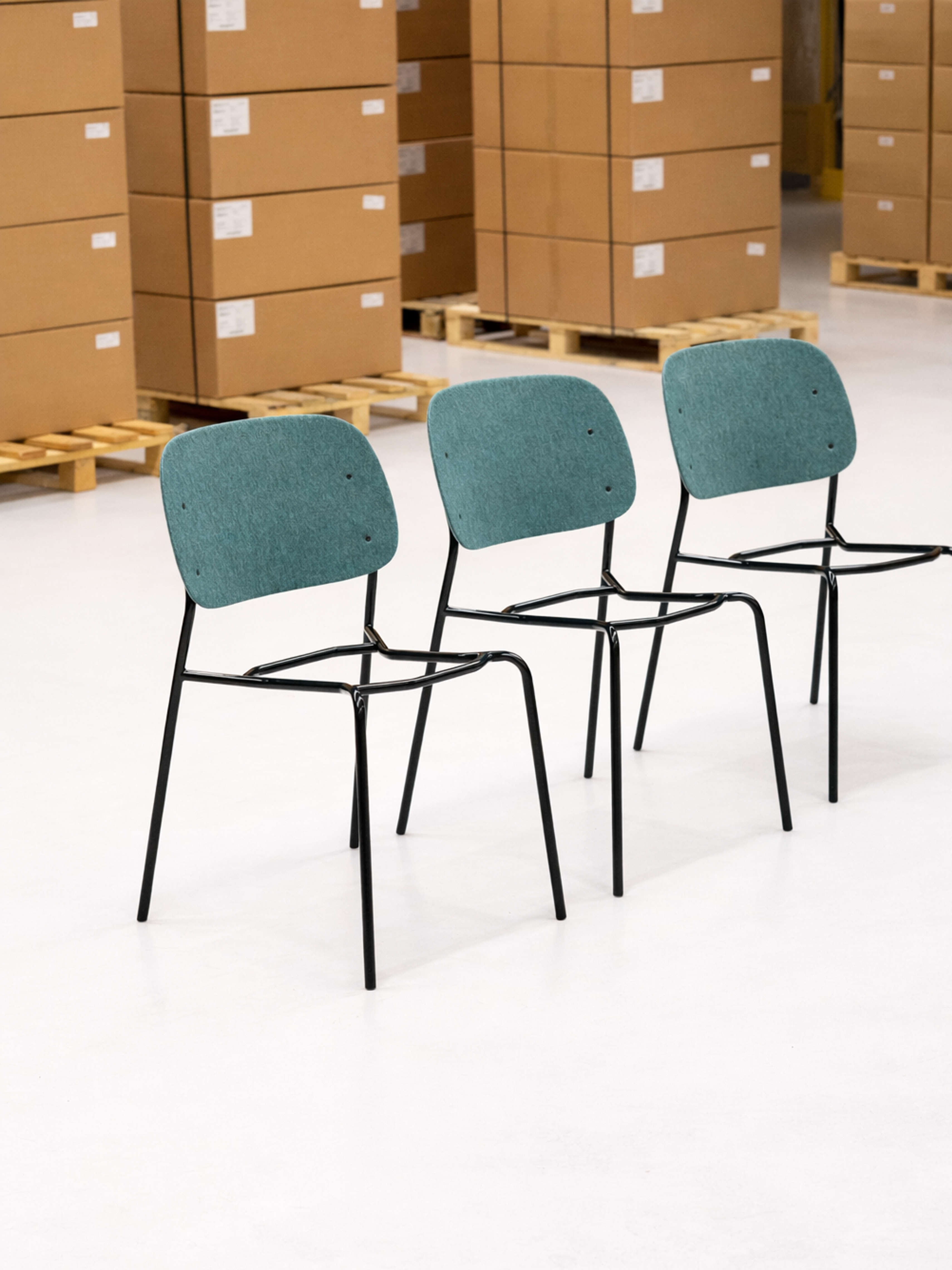 Three Hale Stack Chairs with dark green powder-coated steel frames, photographed in a De Vorm warehouse ready for dispatch