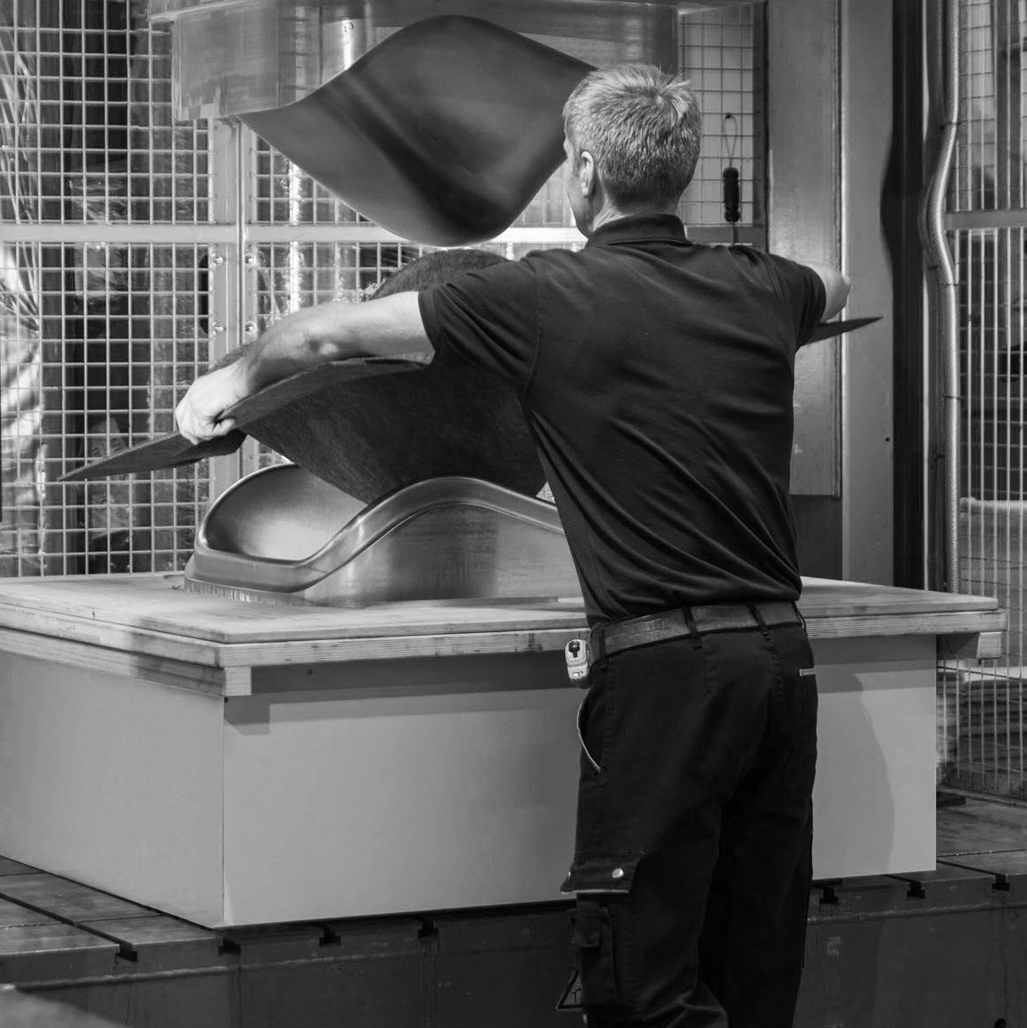 De Vorm production specialist pressing a PET felt chair seat in the factory, black and white