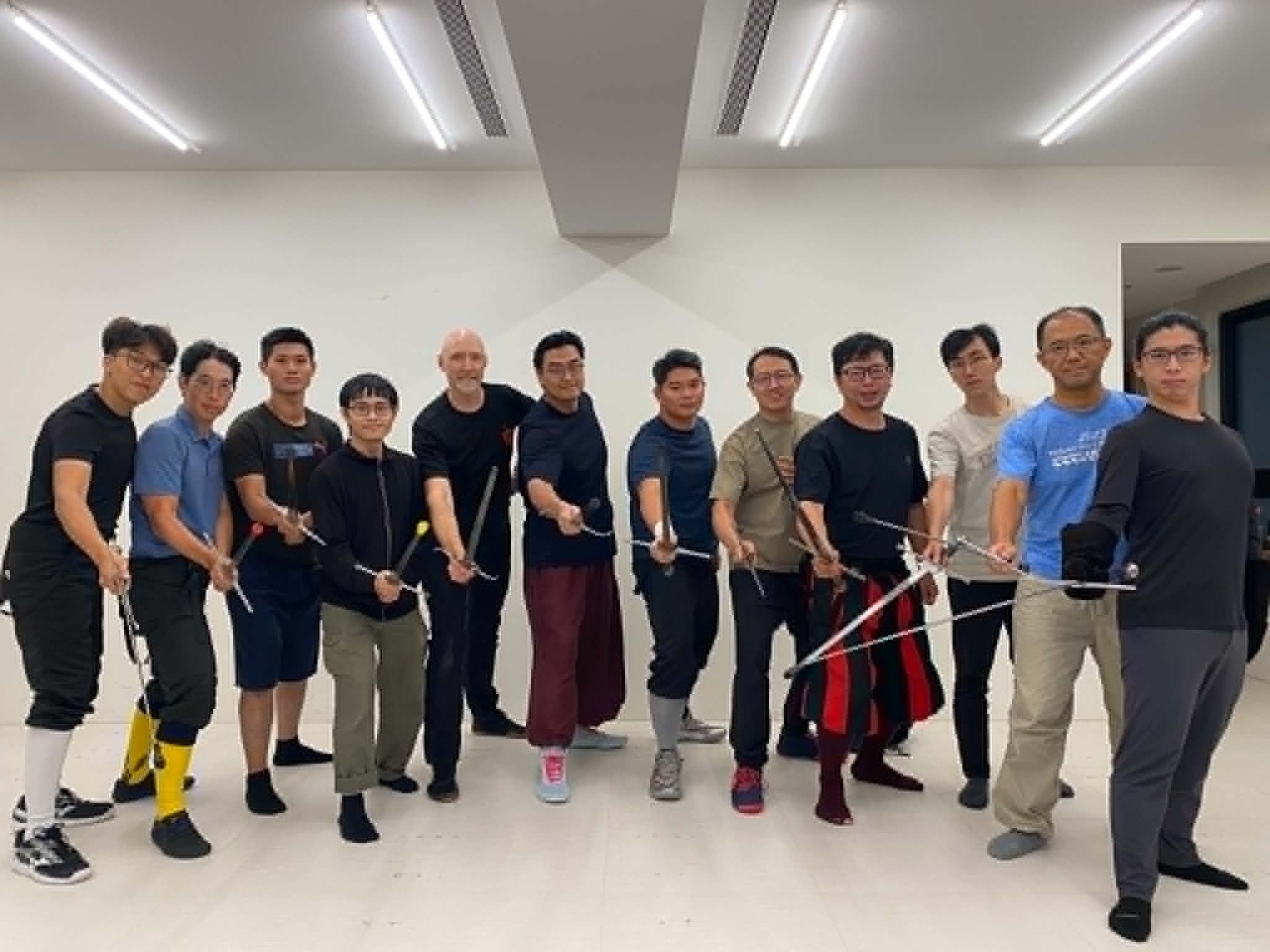 The Taipei intensive group standing in a line, holding their rapiers extended toward the camera