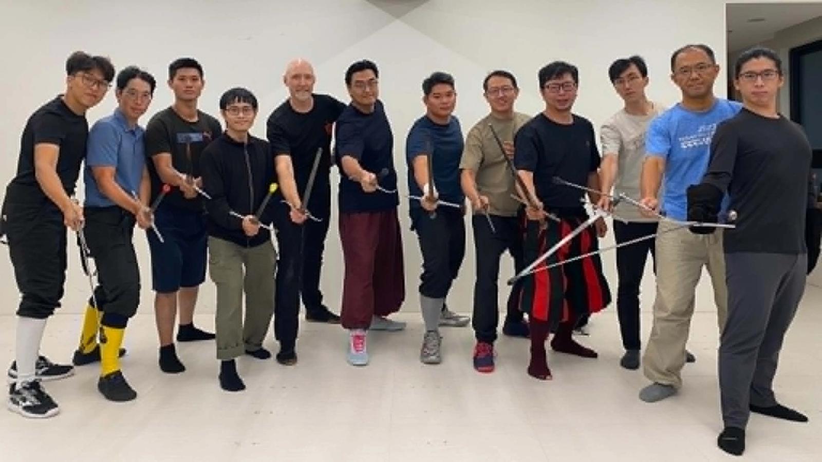 The Taipei intensive group standing in a line, holding their rapiers extended toward the camera