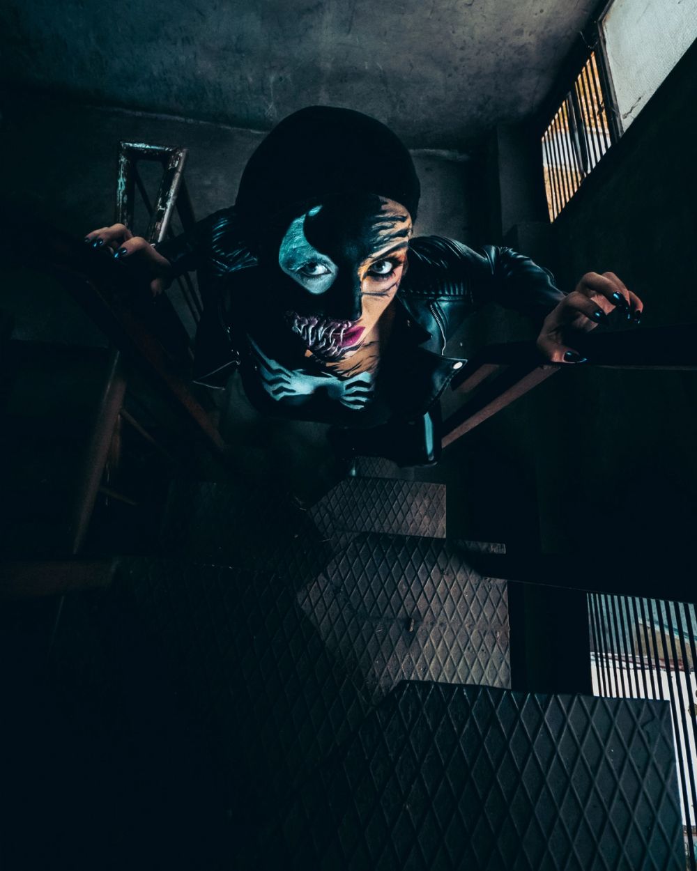 Konceptualni portret žene sa umetničkom maskom i upečatljivim šminkerskim detaljima, fotografisan u industrijskom prostoru sa dramatičnim svetlom i izraženom atmosferom.