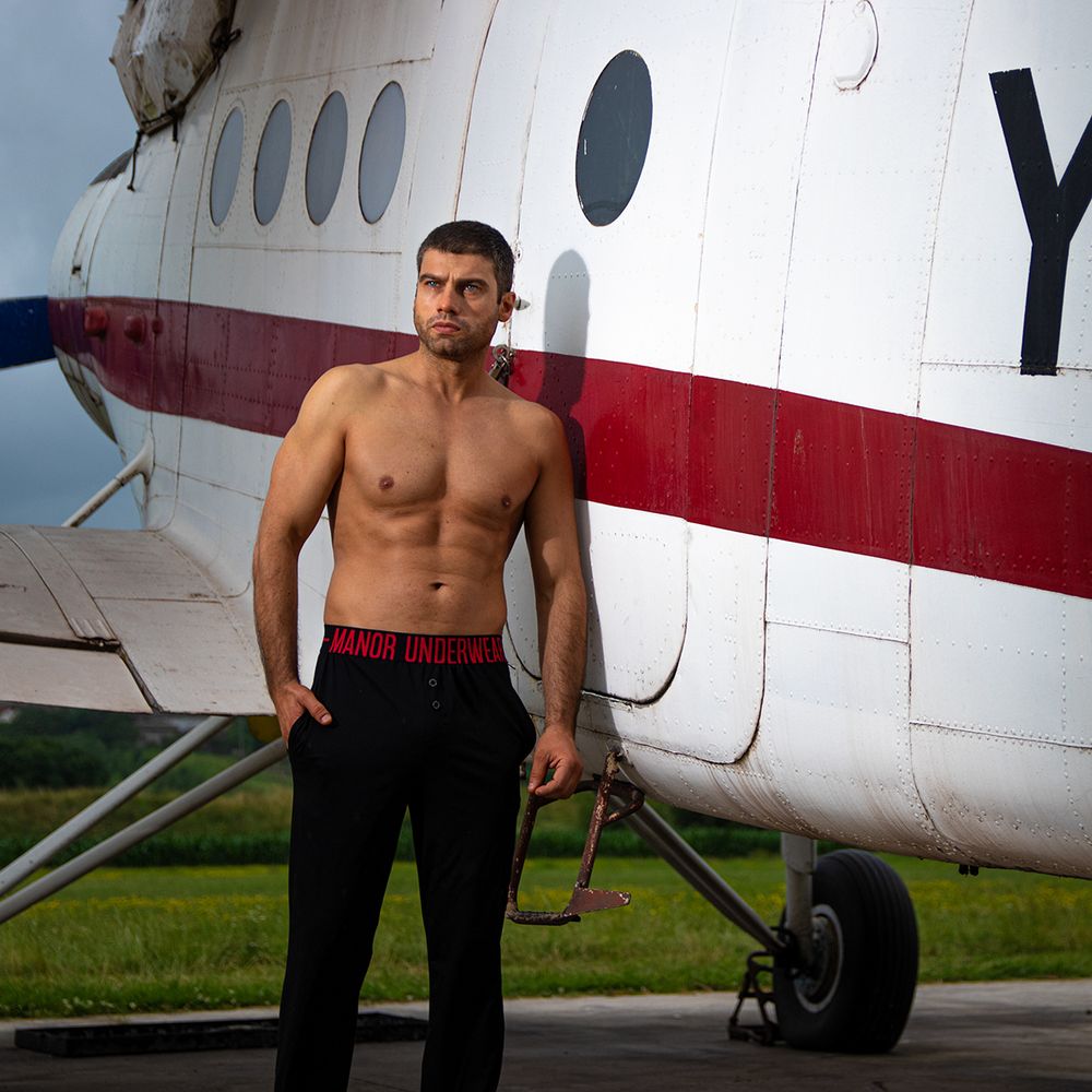 Muški model u donjem vešu i pantalonama ispred aviona, profesionalna underwear fotografija u outdoor kampanjskom okruženju