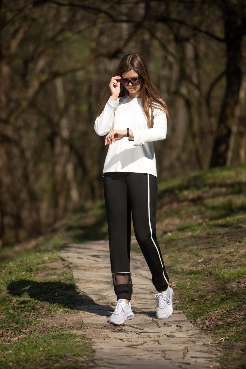 Model u casual outfitu pozira na otvorenom u prirodnom ambijentu, fotografisana u dnevnom svetlu, sa fokusom na udobnost, pokret i lifestyle modni izraz.