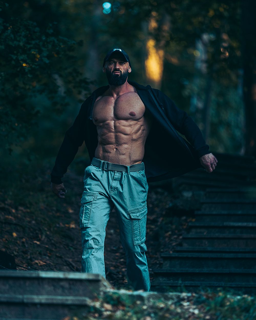 Fitness portret muškarca u pokretu na otvorenom, sa naglašenom mišićnom definicijom, snimljen u prirodnom okruženju, uz dramatično osvetljenje i fokus na snagu, dinamiku i fizičku spremu.