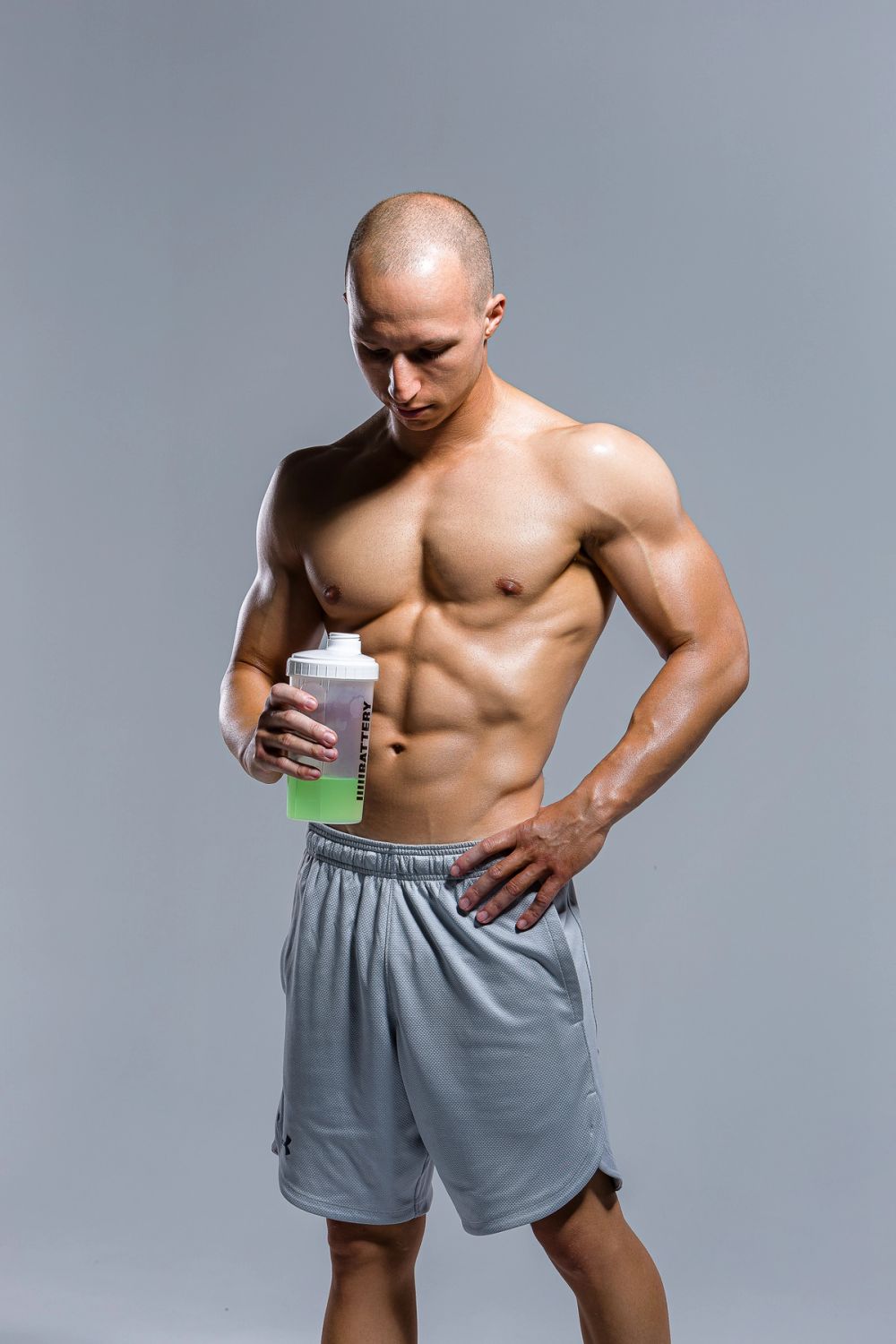 Studio fitness portret muškarca sa naglašenom mišićnom definicijom, snimljen na neutralnoj pozadini tokom pauze nakon treninga, sa fokusom na kontrolu, oporavak i fizičku formu.