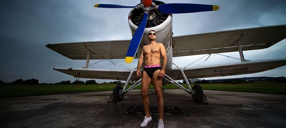 Muški model u slipovima ispred aviona na pisti, profesionalna underwear fotografija muškog donjeg veša u outdoor okruženju