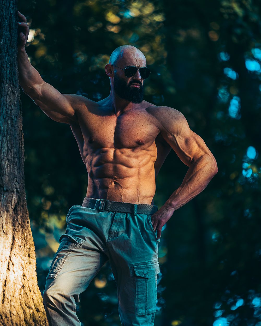 Fitness portret muškarca na otvorenom, sa naglašenom mišićnom definicijom, snimljen u prirodnom okruženju, uz snažno kontrastno osvetljenje i fokus na snagu, stabilnost i fizičku spremu.