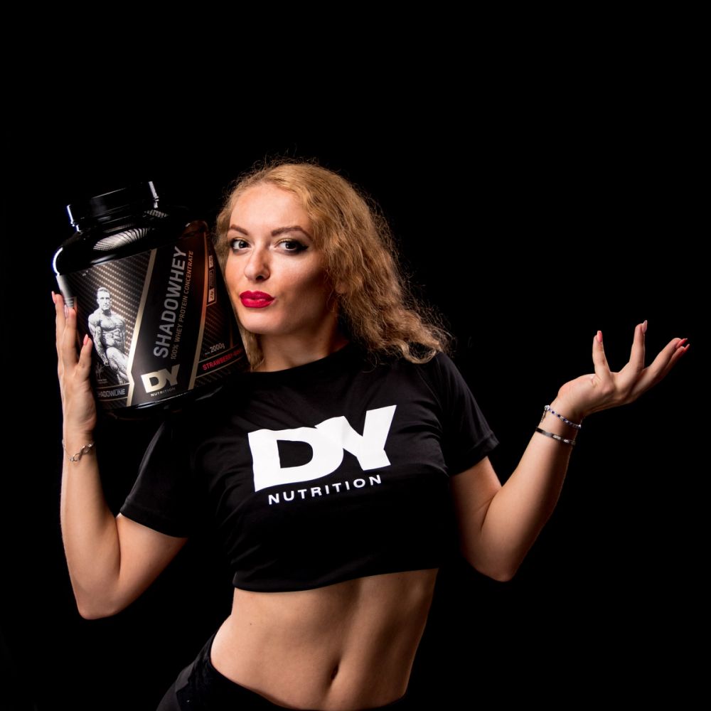 Lifestyle produkt fotografija fitness suplementa sa modelom, koja ističe brend, energiju i samopouzdanje, uz studijsko osvetljenje i čistu crnu pozadinu.