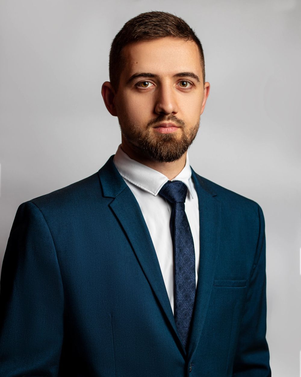 Studijski portret muškarca u poslovnoj odevnoj kombinaciji, fotografisan na neutralnoj pozadini sa kontrolisanim svetlom i naglaskom na profesionalan izraz i čistu kompoziciju.